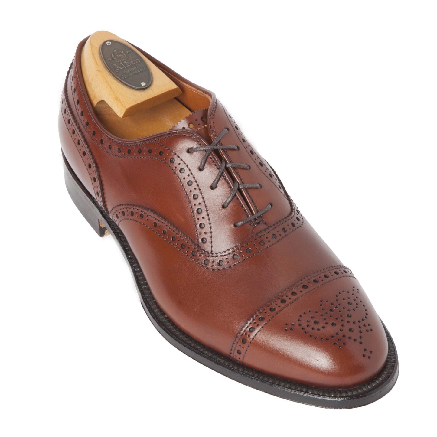 Alden Madisons 911 Burnished Tan Medallion Cap Toe Bal is a polished brown leather dress shoe in burnished tan calfskin, featuring decorative perforations, a lace-up design on the Hampton Last, a leather sole, and includes a wooden shoe tree.