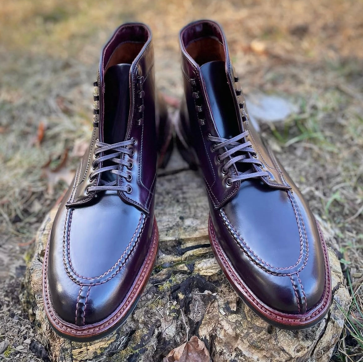 Alden Madisons 40218HC - NST Tanker Boot in Color 8 Shell Cordovan features detailed stitching and a Commando Sole; the shiny dark burgundy boots are shown laced and outdoors on a tree stump with grass and leaves around.