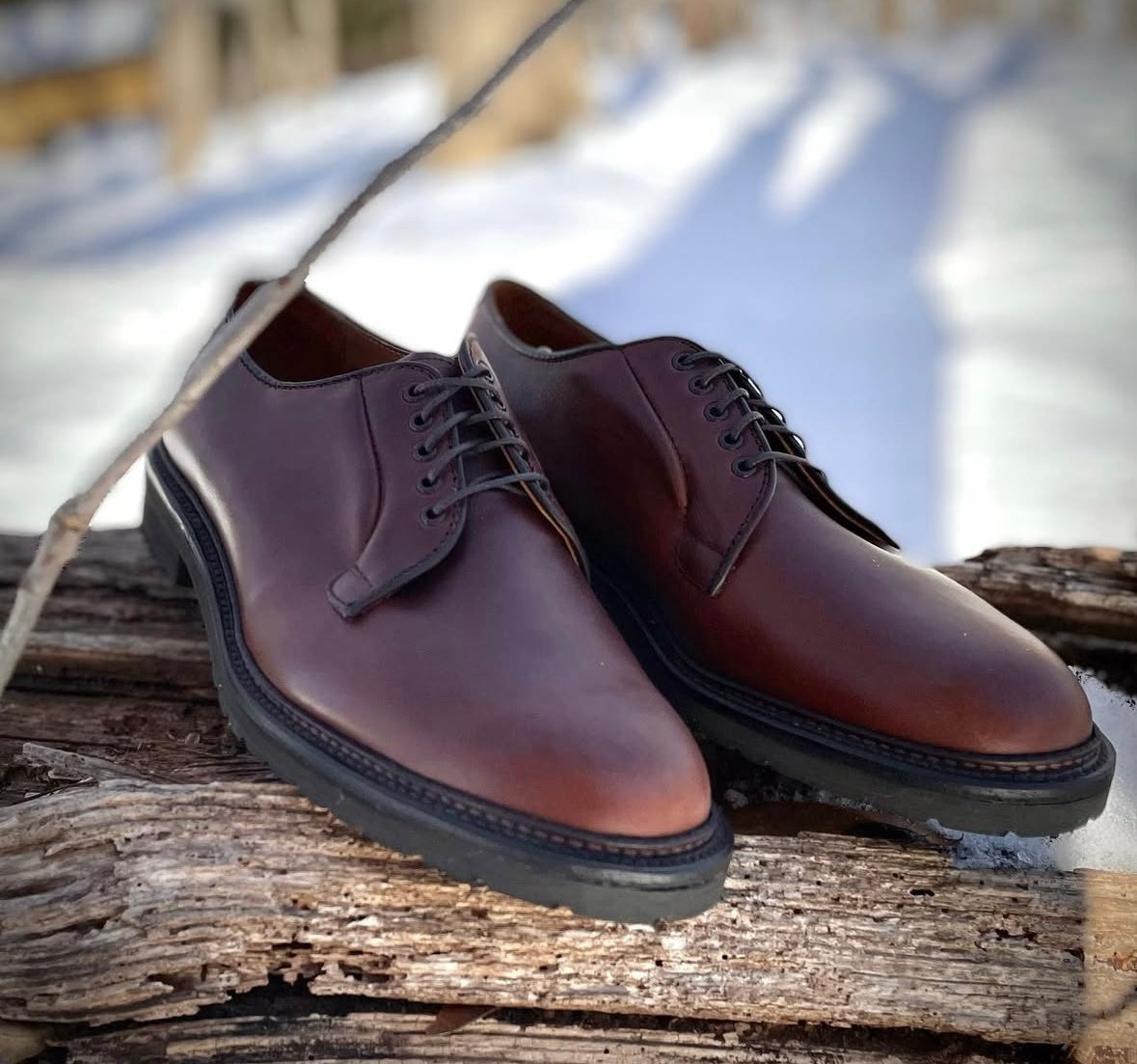 The Alden Madison 9432S Plain Toe Blucher in Brown Chromexcel, featuring Lug Rubber Soles and a Barrie last, is displayed outdoors on a weathered wooden surface with snow in the background.
