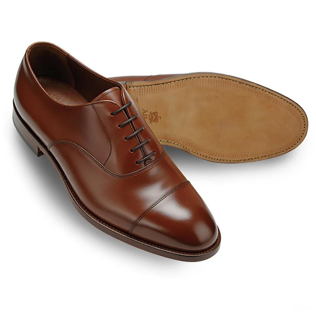 A pair of ALDEN SHOES D5310 Straight Tip Oxford in Madison Brown Calf, one upright to show the cap toe and laces, the other on its side to display the smooth calfskin sole crafted on the Hampton Last.