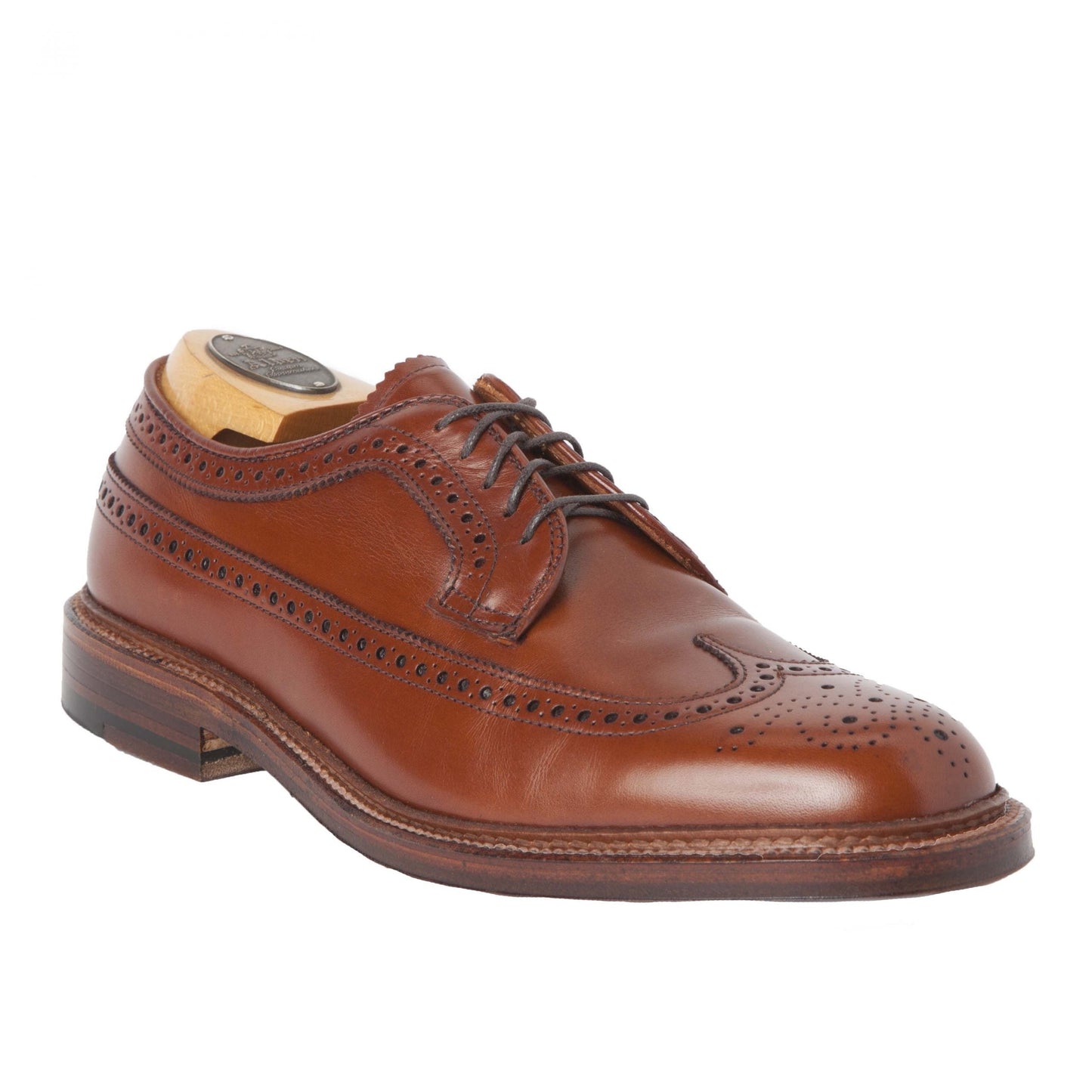 The Alden Madison 979 - Long Wing Blucher in burnished tan calfskin showcases intricate perforations on a brown leather wingtip, set against a white background. A wooden shoe tree maintains its form, featuring a double oak leather outsole and crafted on the Barrie last.