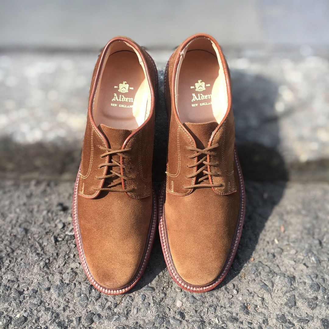 A pair of Alden Madison 29336F Unlined Plain Toe Dover Snuff Suede lace-up shoes with a Flex Leather Sole are placed side by side on a gray textured surface, sunlight highlighting their smooth suede finish and details.