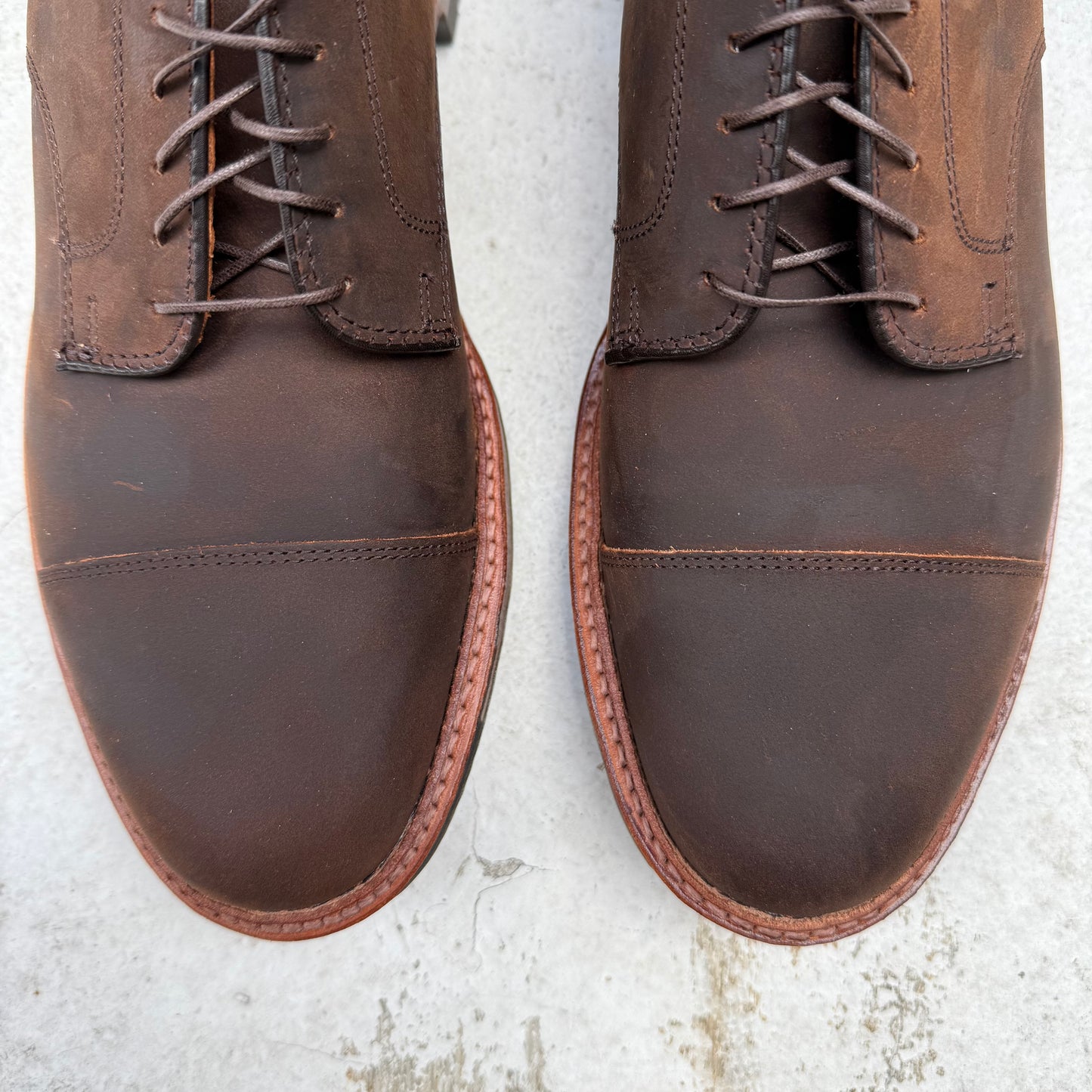 A close-up of Alden Madisons D4519C - Tobacco Chamois Cap Toe Blucher boots on a light surface showcases detailed stitching and laces. The rich, polished finish and sturdy Commando Sole highlight their exceptional craftsmanship.