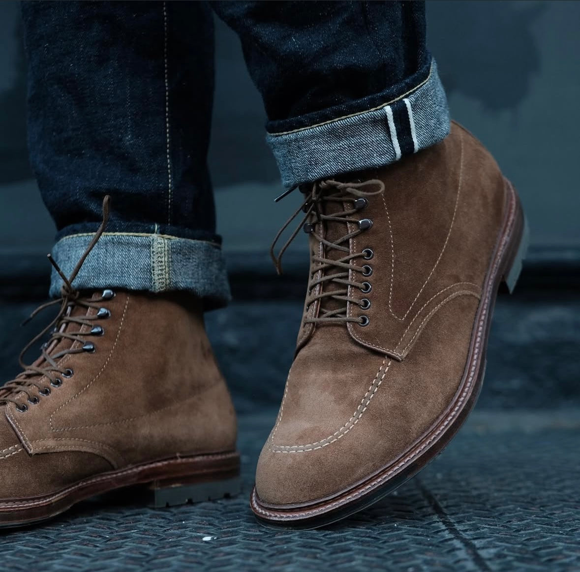 Close-up of a person wearing Alden Madison 4011HC Indy Boot in snuff suede with antique commando sole and dark cuffed jeans, standing on a textured metal surface.