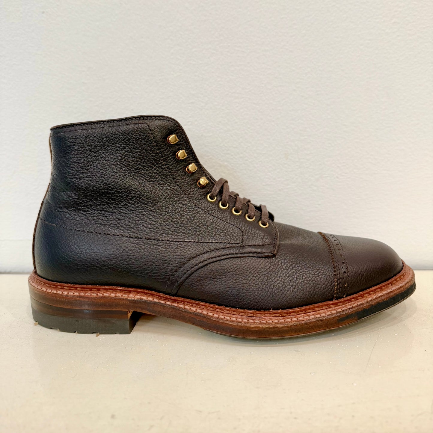 The Alden Madison D9819HC - Jumper Boot in Regina Brown Grain is a single brown calfskin leather boot featuring a textured surface, cap toe, brass eyelets, brown laces, sturdy midsole, and black Commando sole. The elegant boot is displayed against an off-white background.