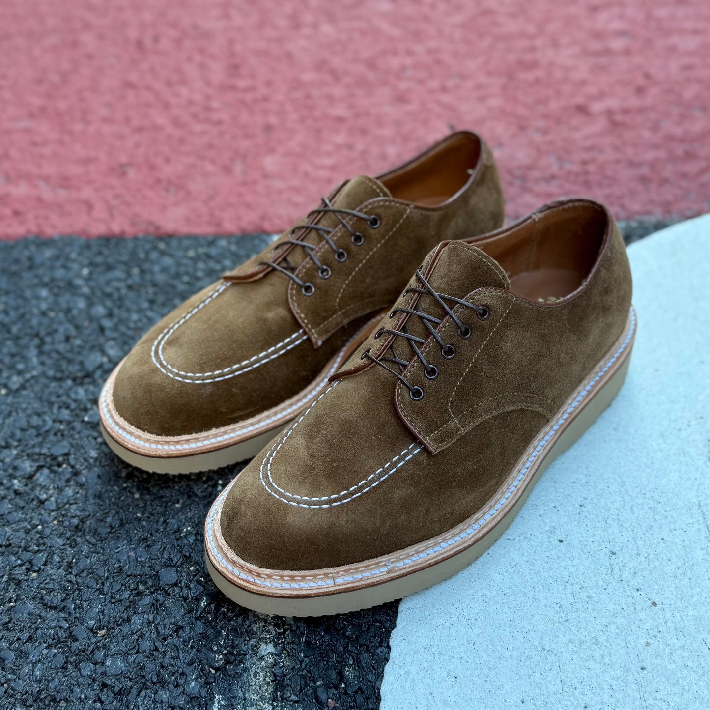 The ALDEN SHOES M7601Y - Snuff Suede Indy Shoe with Wedge features white-stitched derby styling on thick beige soles, dark brown laces, and a moc toe. Designed on the Trubalance Last for comfort, they rest on a tricolored black, red, and white surface.