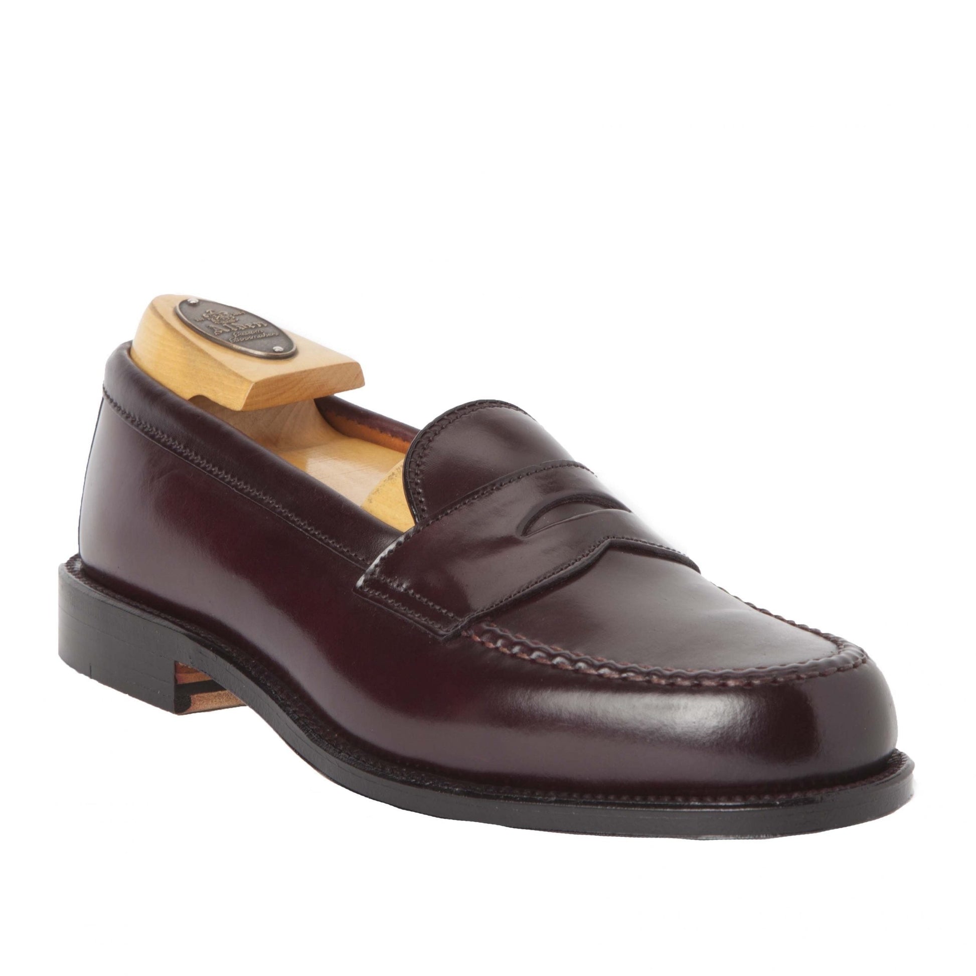 The 986 - Leisure Hand Sewn by Alden Madison is a dark brown leather loafer with a penny strap and detailed stitching on a white background. It boasts a black premium leather sole, showcasing exquisite craftsmanship with a wooden shoe tree maintaining its shape.