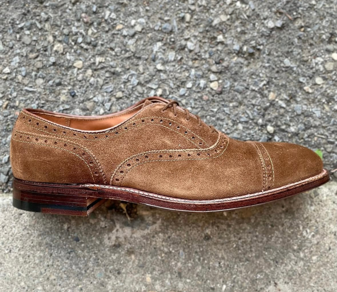 A single Alden Madison 51670F Medallion Cap Toe Bal in Snuff Suede, crafted on the Hampton Last with a Flex leather sole, features brogue detailing and rests on a rough textured outdoor surface.
