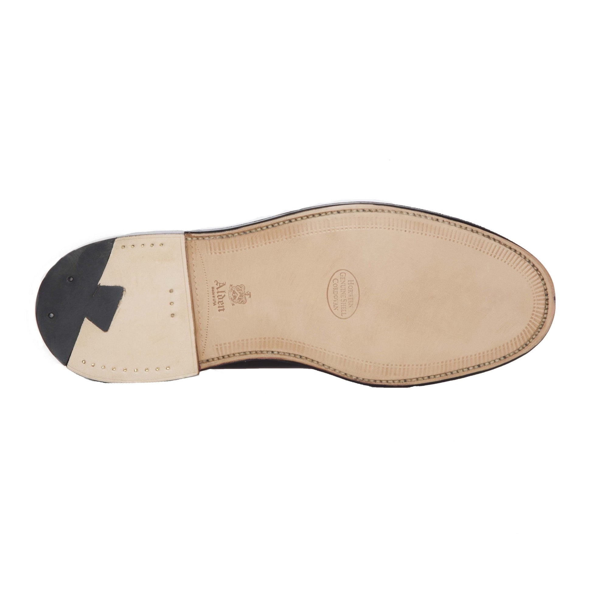 The image showcases the elegant sole of an Alden Madison 986 - Leisure Hand Sewn in Color 8 Shell Cordovan shoe, accentuated by a tan finish with black heel details. Embossed text and a logo embellish the arch and heel tip, with small nails artistically arranged around the heel area.