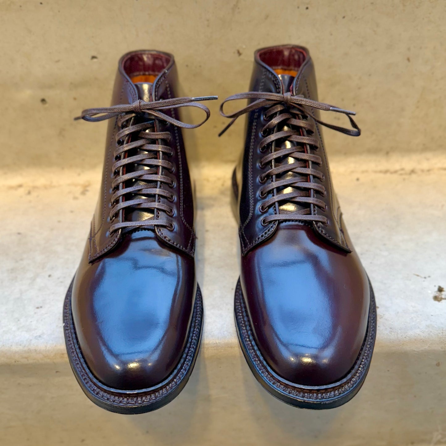 A pair of Alden Madisons 45168 - Plain Toe Director Boots in Color 8 Shell Cordovan, showcasing their sleek design and glossy finish, rests side by side on a light gray surface.