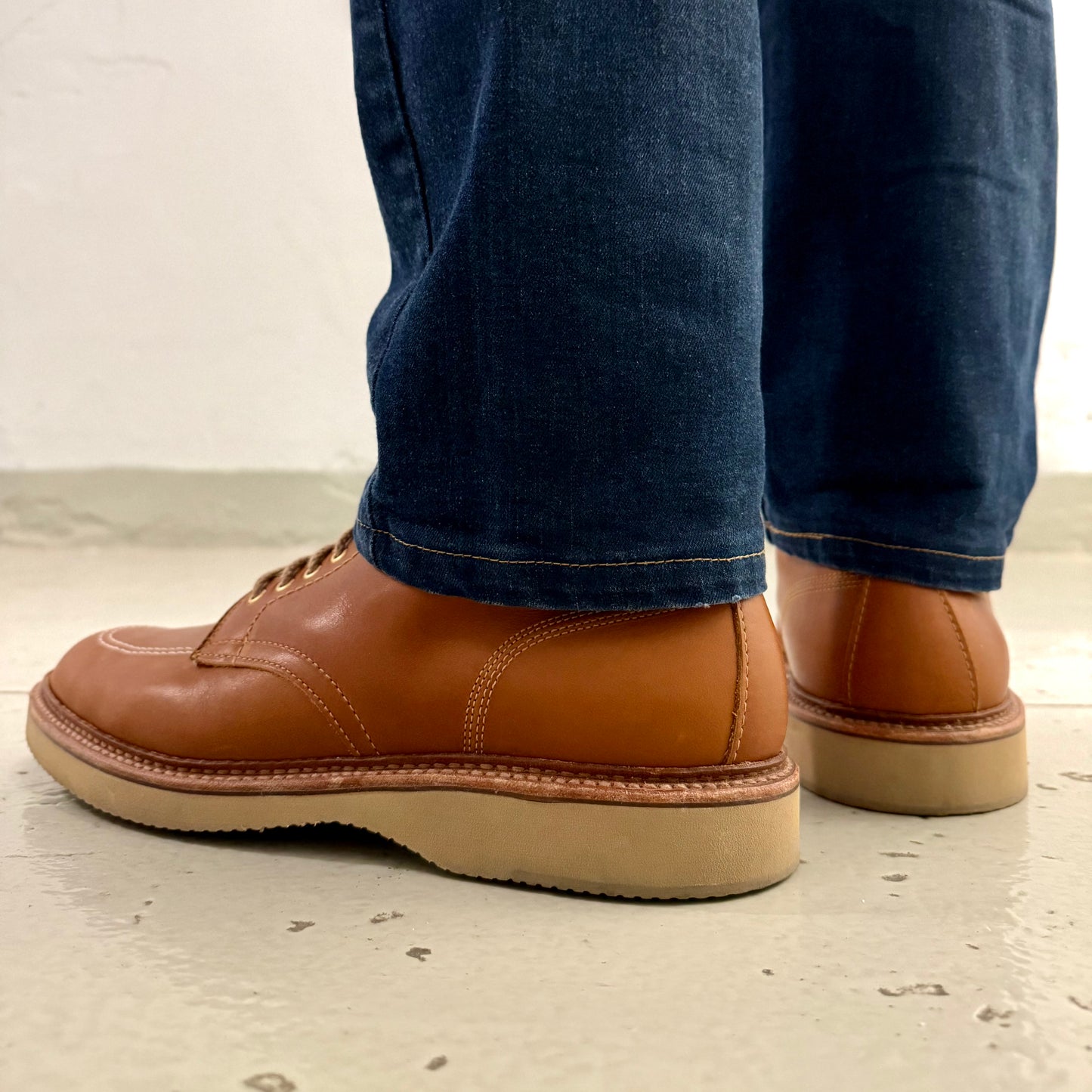 A person stands on a light-colored floor, wearing stylish 40311H Sherwood Indy Boots by Alden Madison, crafted from Saddle Calf Leather and paired with blue jeans. The focus highlights the casual footwear and finely stitched hems, emphasizing both comfort and elegance.