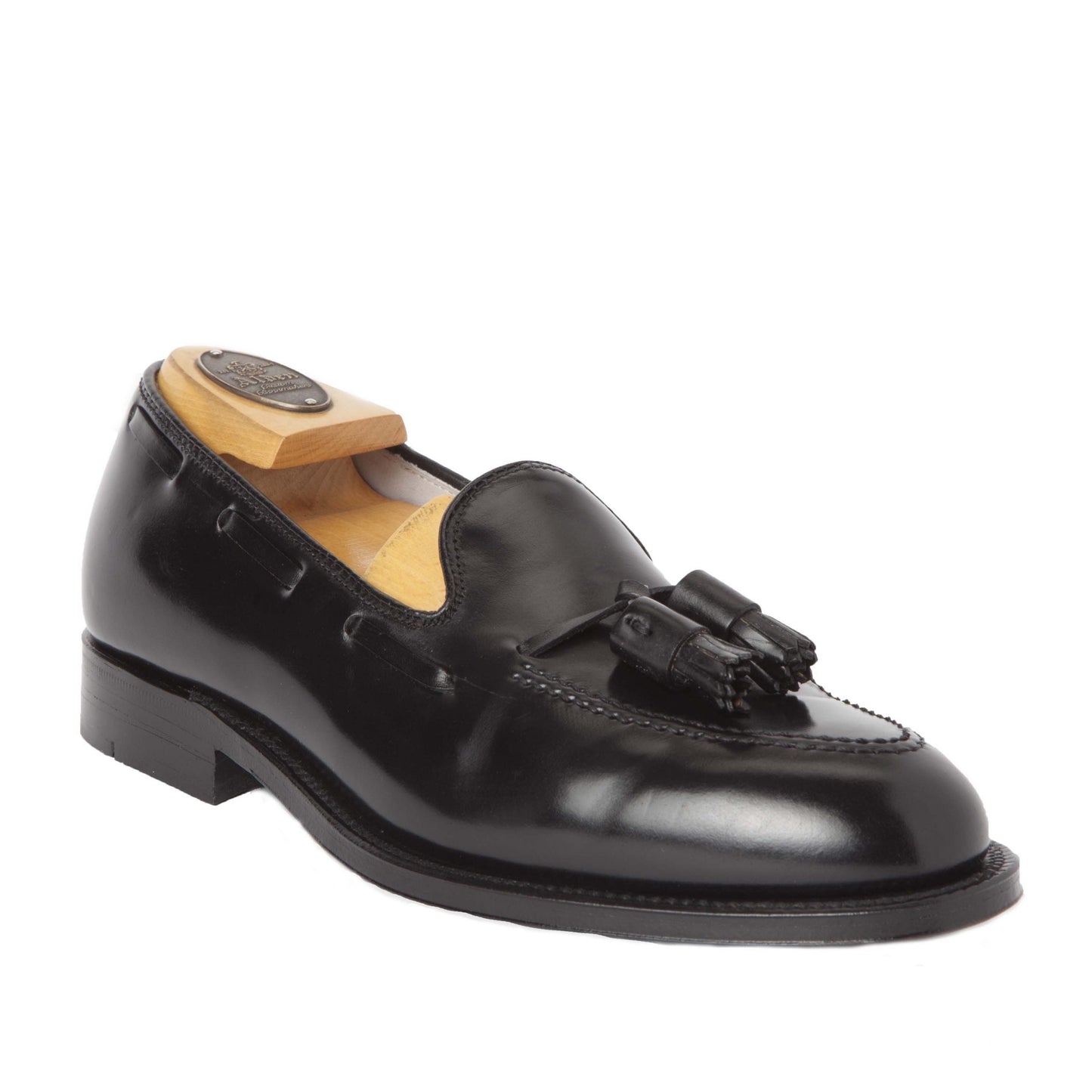 The Alden Madison 664 Tassel Loafer, crafted in polished Black Shell Cordovan, features a rounded toe and low heel on an Aberdeen Last. It includes a wooden shoe tree and decorative tassels on the upper front, finished with a high-quality leather black sole for durability.