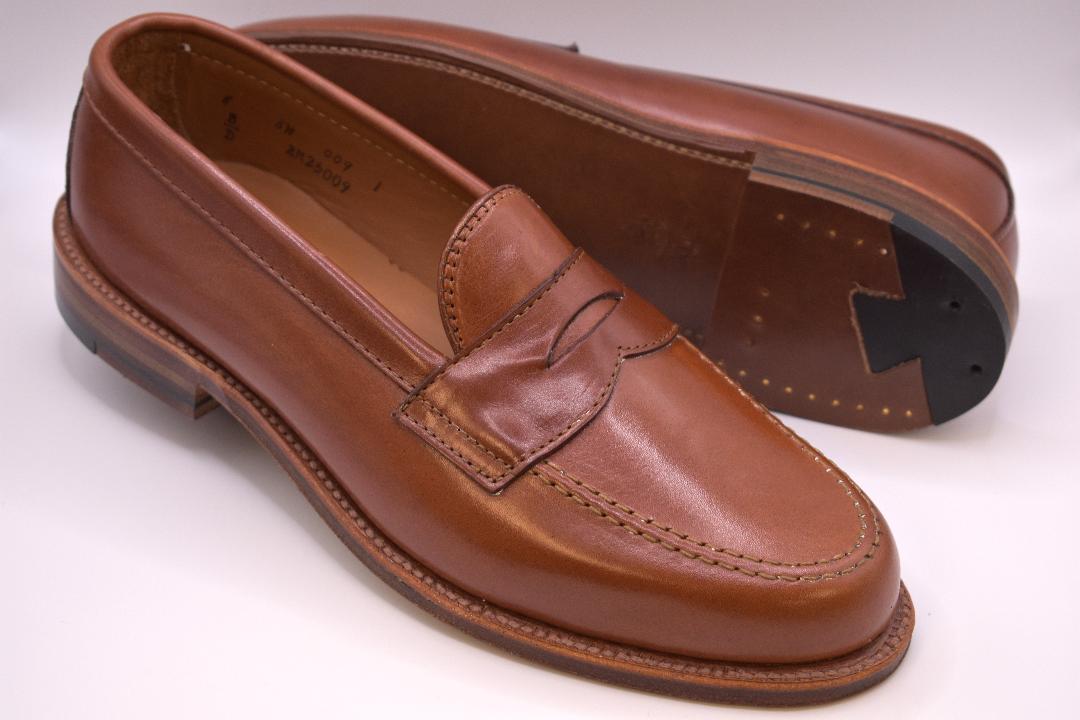 A pair of Alden Madison 9823 - Penny Loafer in Tan Michigan Calf; one shoe stands upright showing the top and side, while the other lies on its side, revealing the Flex Oiled Leather Sole and intricate stitching details.