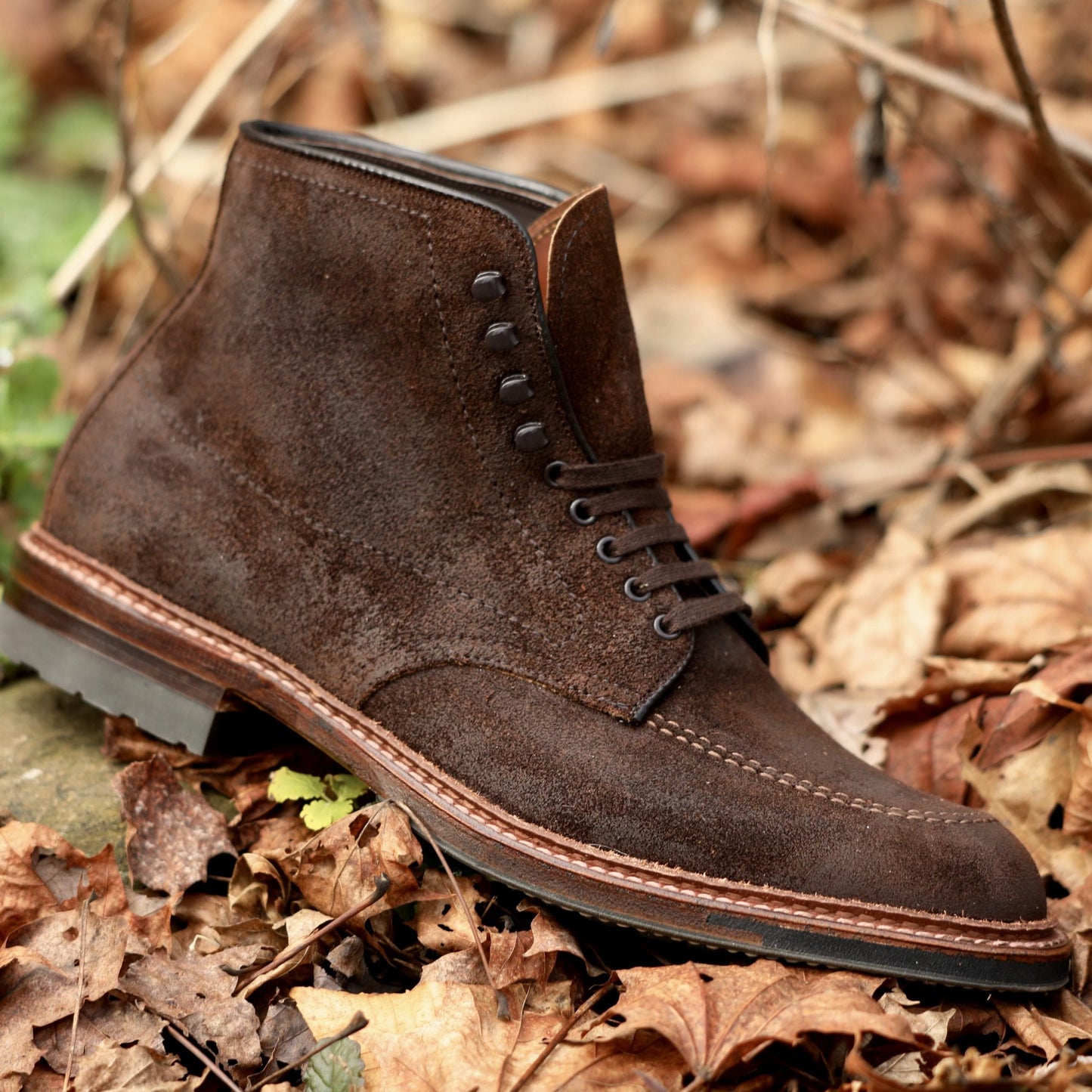 Alden Madisons 4015HC Indy Boot in Tobacco Reverse Chamois, with dark eyelets and laces, sits on fallen autumn leaves. Its stitched commando sole and rich suede texture beautifully complement the earthy tones.