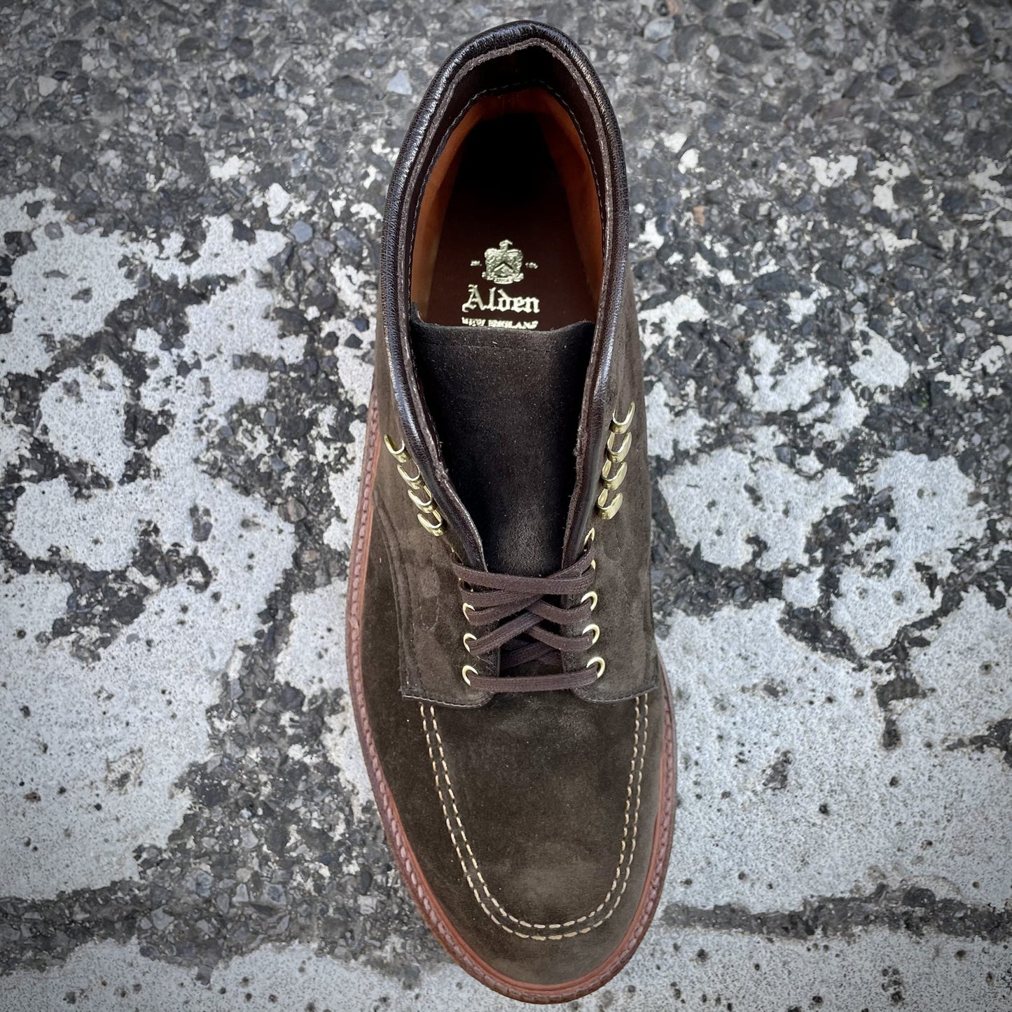 A single D0938H - Duncan Indy Boot in Loden Suede, branded Alden Madison on the insole and laced with dark brown strings, crafted on the Truebalance Last, is positioned on a textured, cracked concrete surface.