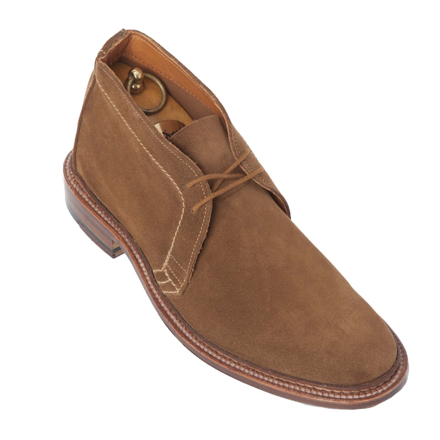 The Alden Madison 1493 Unlined Chukka in Snuff Suede showcases clean stitching and matching laces on the Leydon Last, with a wooden shoe tree inside, and rests on a single flex leather sole, elegantly set against a white background.