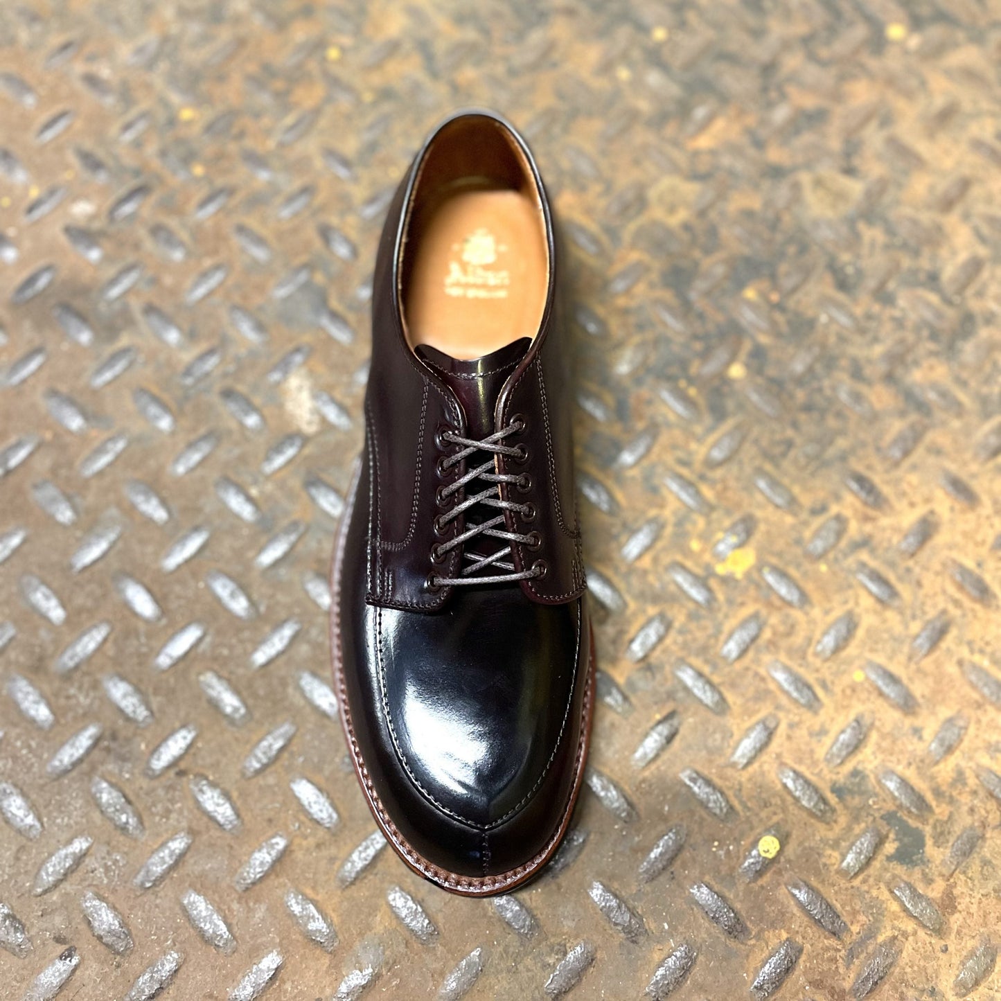 An Alden Madison D1629C - V Tip Split Toe Blucher in Color 8 Shell, with a polished toe and detailed sole stitching, sits on a textured metal surface. This dark brown leather shoe features laces and a rugged Commando Sole for enhanced durability.