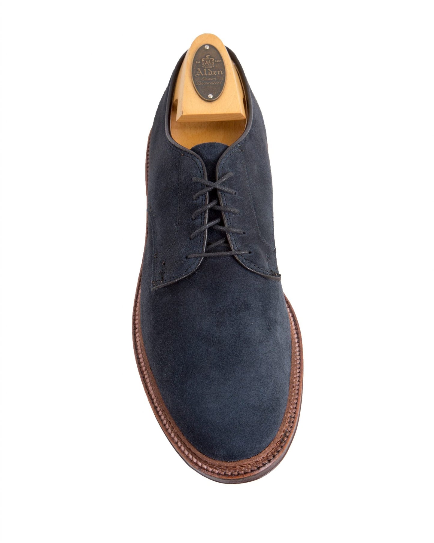 The Alden Madison 29331F Unlined Plain Toe Blucher in blue suede features black laces, a storm welt, and a brown flex leather sole with edge stitching. It includes a branded wooden shoe tree for added elegance and durability.