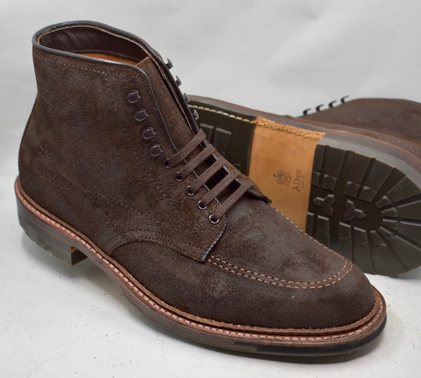 Alden Madisons 4015HC - Indy Boot in Tobacco Reverse Chamois is shown with dark laces and detailed stitching. One boot leans against the other, highlighting its sturdy Commando Sole with intricate tread and a visible brand logo.