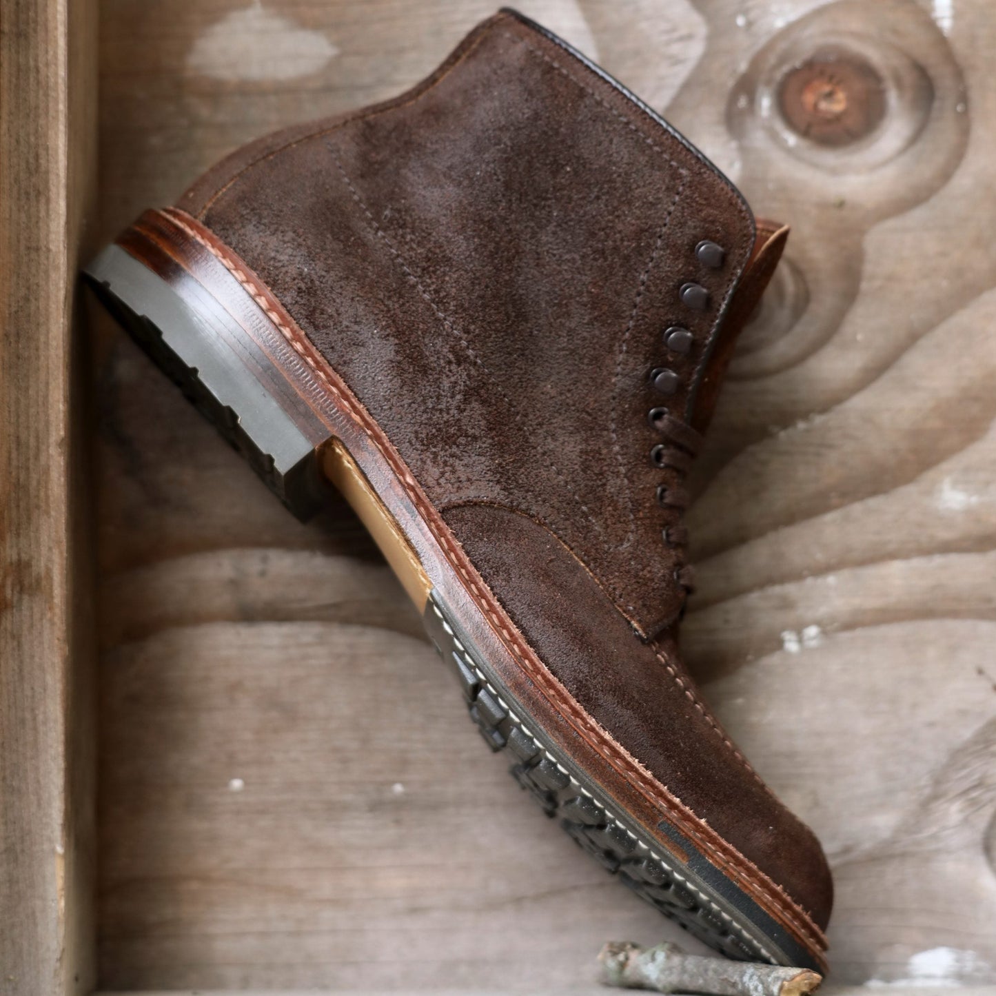 A single Alden Madison 4015HC - Indy Boot in Tobacco Reverse Chamois rests against a wooden backdrop, featuring decorative stitching, metallic eyelets, and a rugged Commando Sole for ultimate traction.