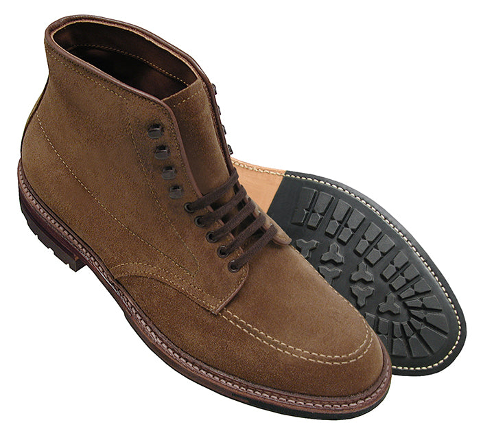 The Alden Madison 4011HC - Indy Boot features snuff suede lace-up design, black rubber soles, and a durable storm welt. One boot stands upright while the other lies on its side, highlighting the tread pattern. They have brown stitching and six eyelets for laces.