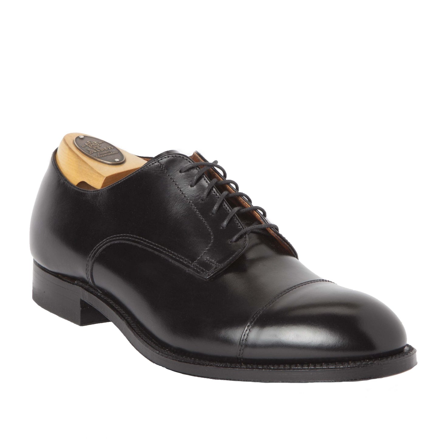 The Alden Madison 558 - Modified Cap Toe Blucher in black calfskin features a polished, cap toe design with dark laces. Displayed on a wooden shoe tree, it highlights its sleek and classic style with a single oak leather sole for durability.