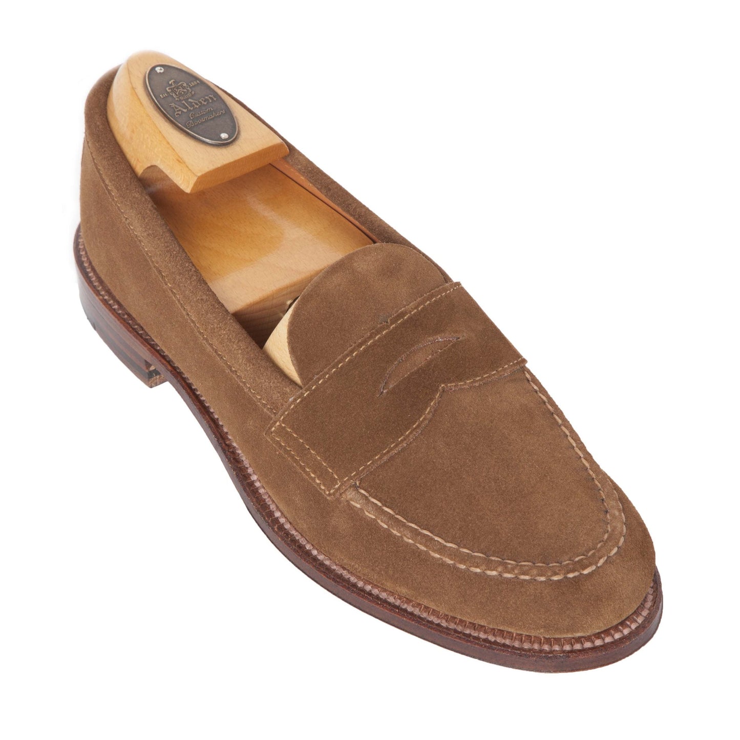 The 6243F - Unlined Leisure Hand Sewn in Snuff Suede loafer by Alden Madison is elegantly displayed with a wooden shoe tree, highlighting its refined stitching, penny strap detail, and intricate upper and sole craftsmanship against a white backdrop.