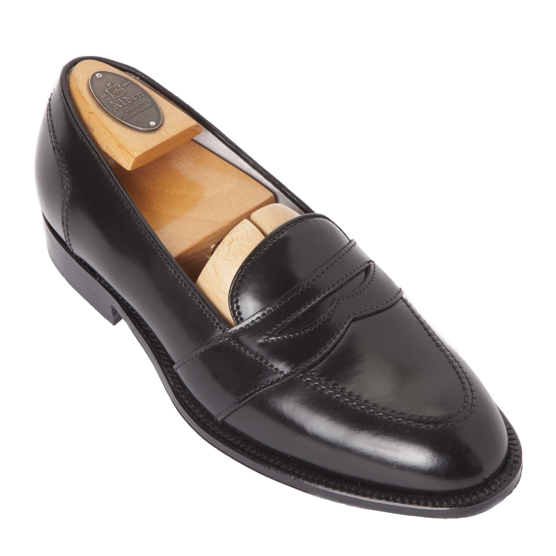 The Alden Madison 6845 Full Strap Loafer, crafted from luxurious Black Shell Cordovan and featuring the classic Aberdeen Last design, is presented with a wooden shoe tree. Its sleek black leather, polished finish, and elegant sole are highlighted alongside side and top views.