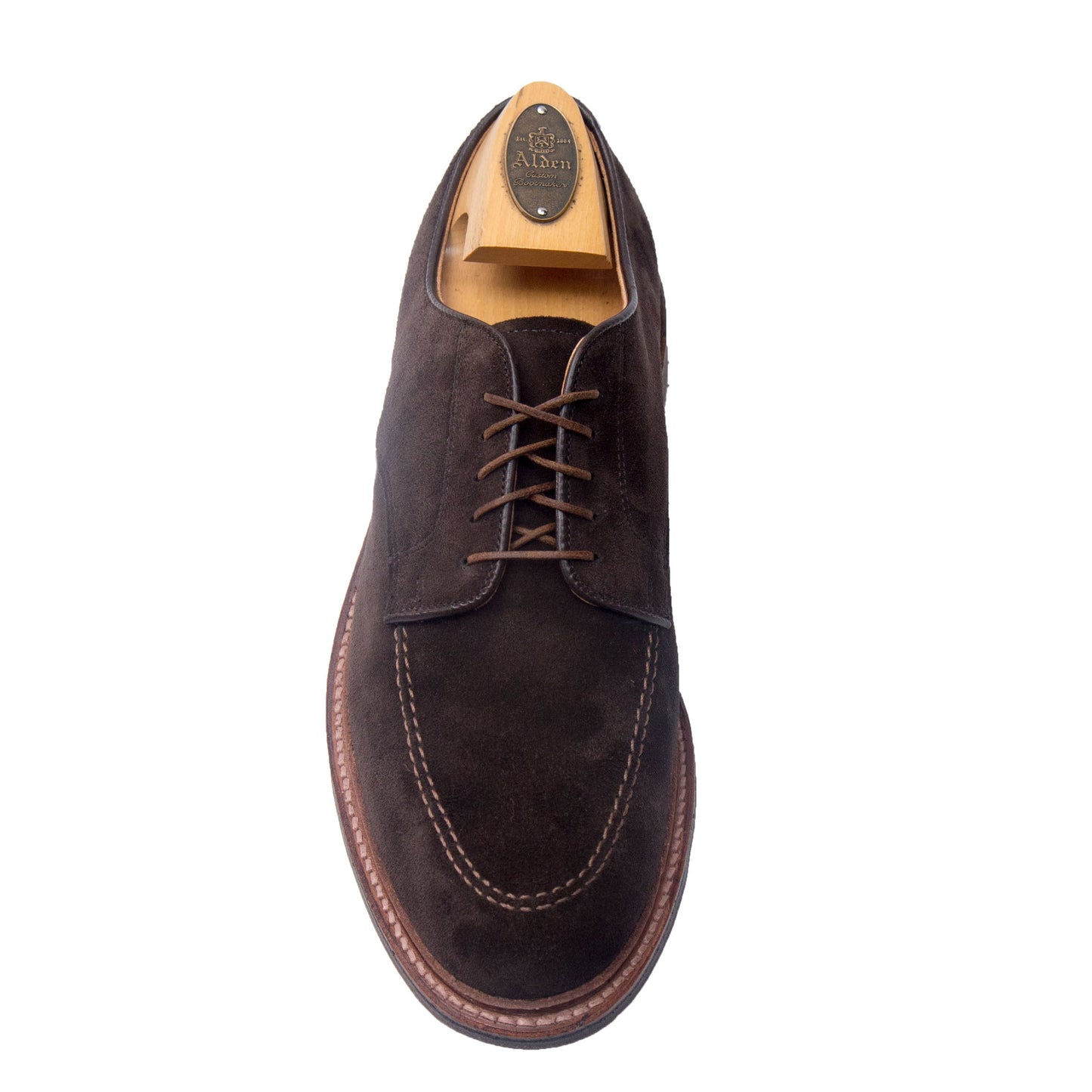 The Alden Madison 704 Mocc Toe Blucher in Brown Suede, featuring brown laces, visible stitching, and a dress rubber sole for comfort and durability, is shown with a wooden shoe tree on a white background.