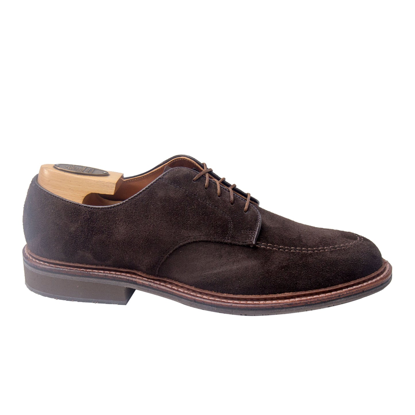 The Alden Madison 704 Mocc Toe Blucher in Brown Suede is a dark brown suede lace-up dress shoe with a rounded toe, sturdy rubber sole, and wooden shoe tree insert, crafted on the Orleans Last.