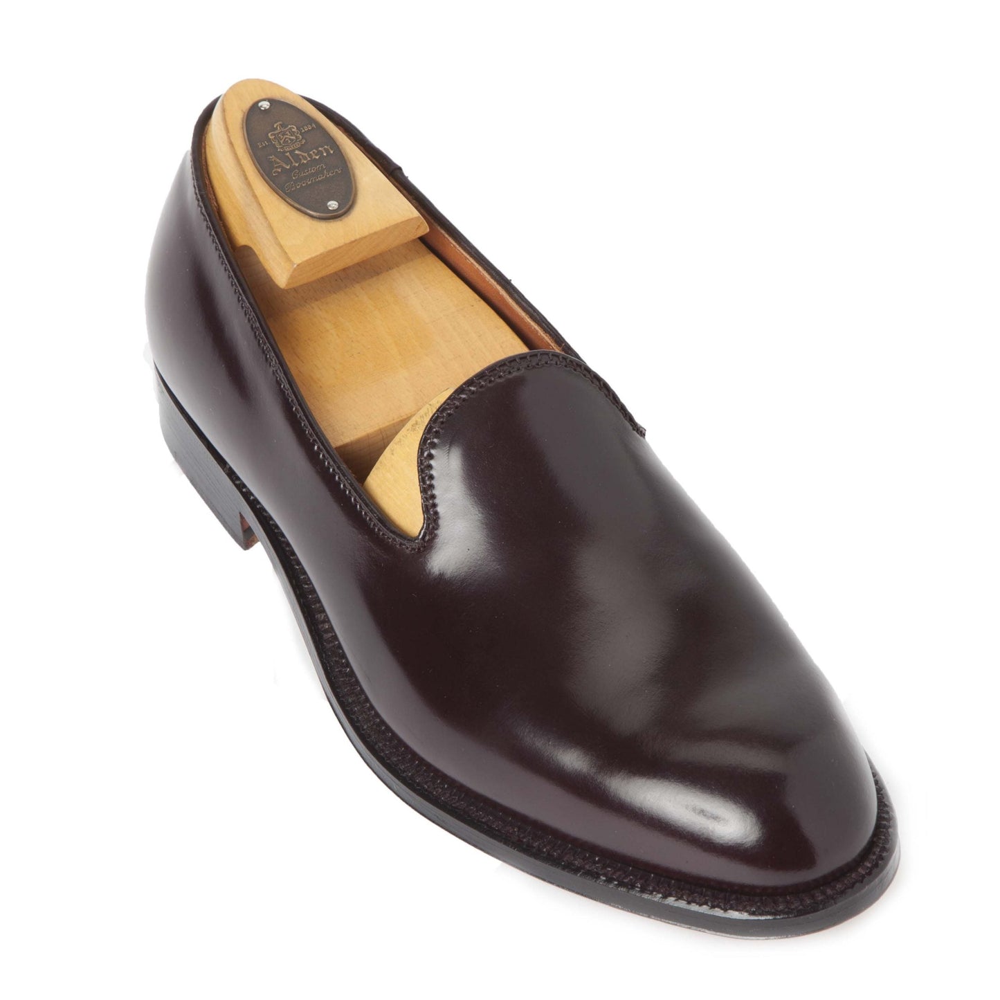 The Alden Madison 8818 – a plain toe slip-on in Color 8 Shell, crafted on the Aberdeen Last – is elegantly displayed with its polished dark brown leather and features a wooden shoe tree, set at an angle against a white background.