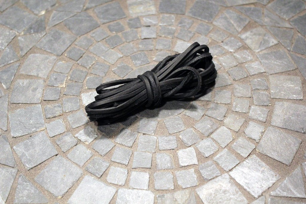 A 74-inch Alden Madison Rawhide Lace in Black, ready to be cut to size, is neatly coiled on a circular gray stone mosaic tile floor.