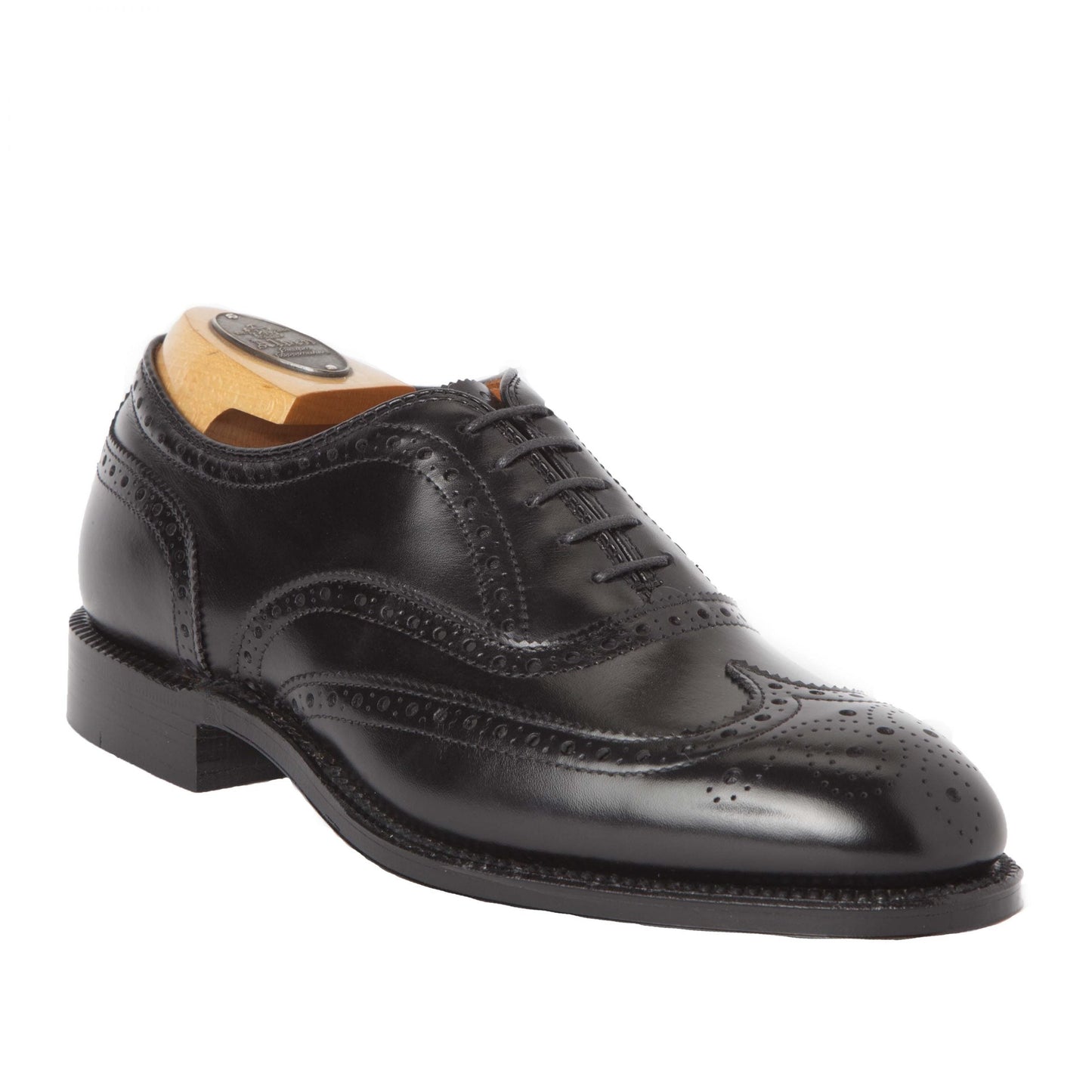 The Alden Madison 903 - Wing Tip in Bal Black Calfskin is shown on a white background with intricate brogue detailing, crafted on the Hampton Last. A leather sole ensures elegance, and a wooden shoe tree maintains its impeccable shape.