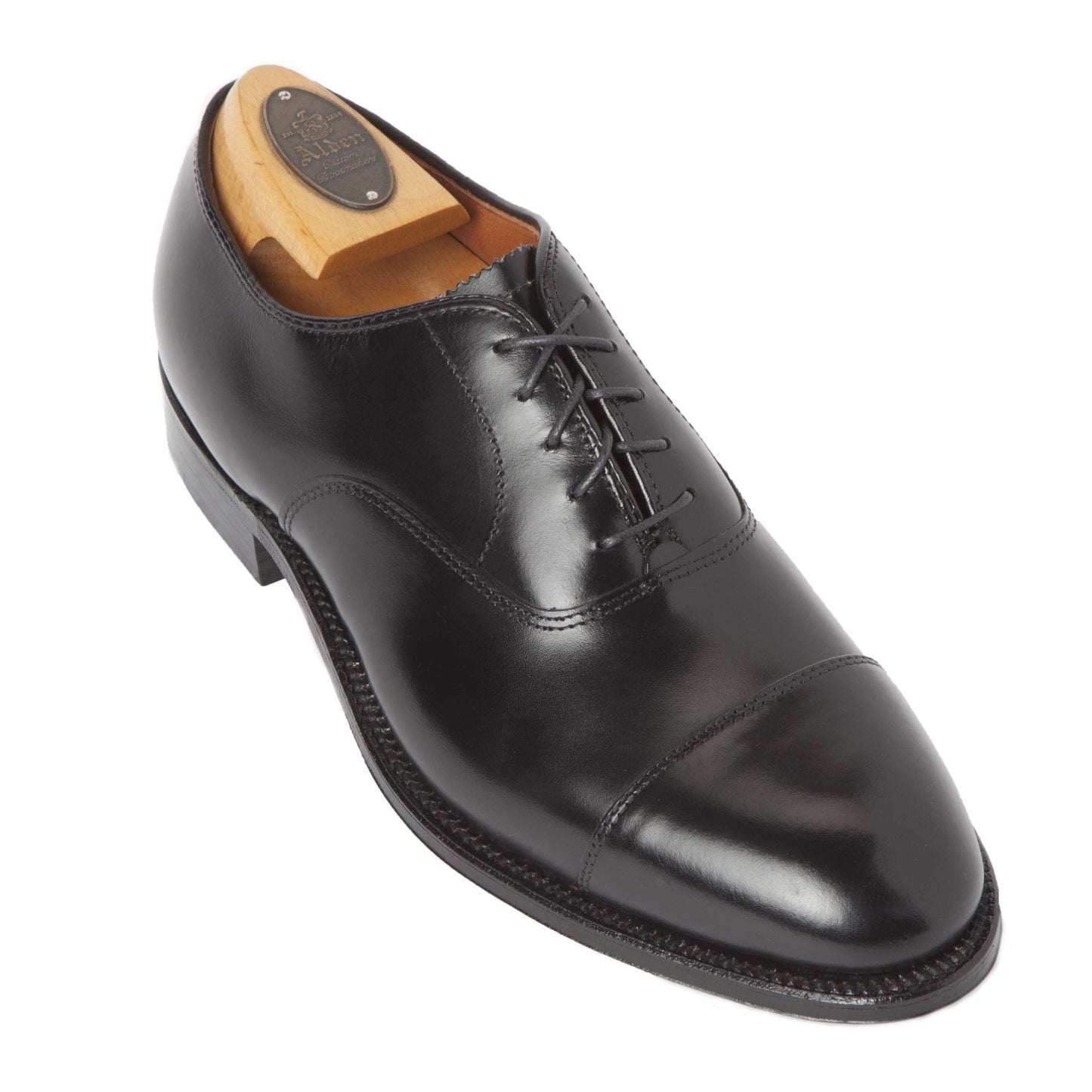 The Alden Madison 907 - Straight Tip Bal in Black Calfskin is a polished Oxford shoe with a cap toe, featuring sleek laces, a wooden shoe tree, and a leather sole. Its elegant design is perfect for formal occasions.