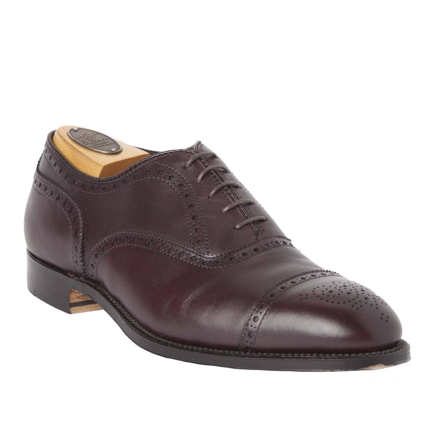 The Medallion Cap Toe Bal by Alden Madison in burgundy calfskin features brogue detailing, a wooden shoe tree, and a rounded toe on the Hampton Last with a leather sole and intricate perforations on the toe cap and seams.