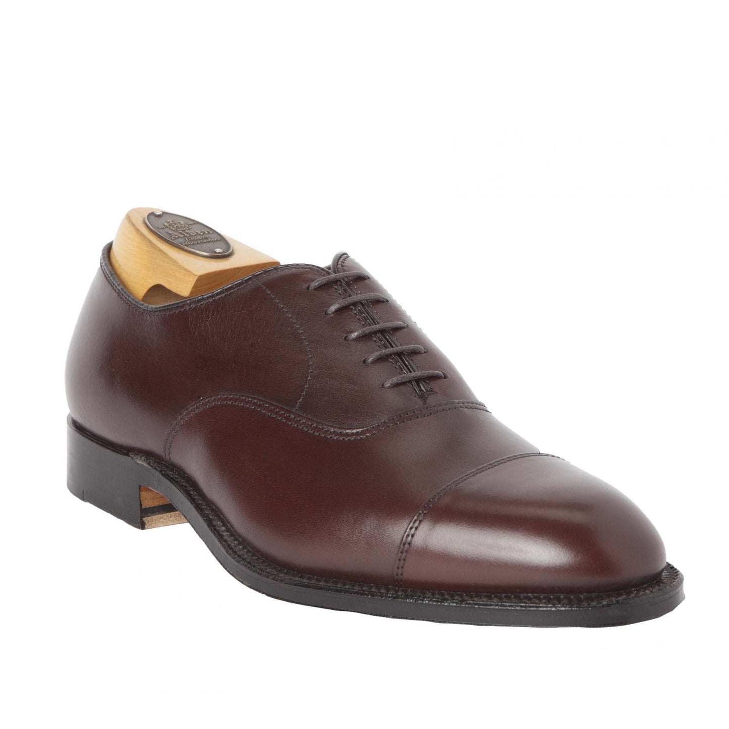 The Alden Madison 920 - Cap Toe Bal in Brown Calfskin, featuring a polished finish, black laces, and a leather sole on the Hampton Last, is elegantly displayed on a wooden shoe tree.