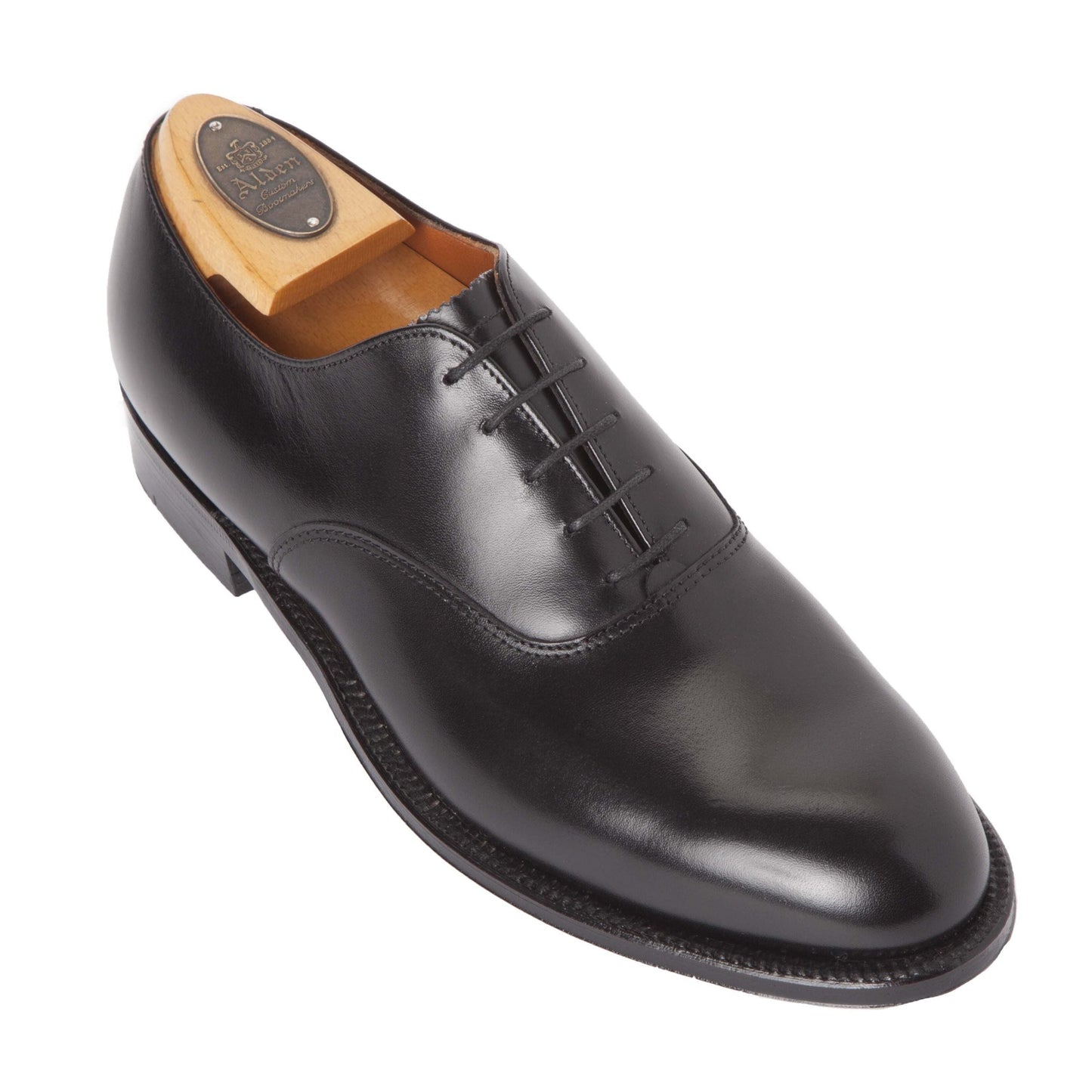 Alden Madisons 932 - Plain Toe Bal in Black Calfskin is a refined Oxford shoe with closed lacing, an exquisite single oak leather sole, and crafted on the Aberdeen last. Displayed with a wooden shoe tree, it sits angled against a plain white background.