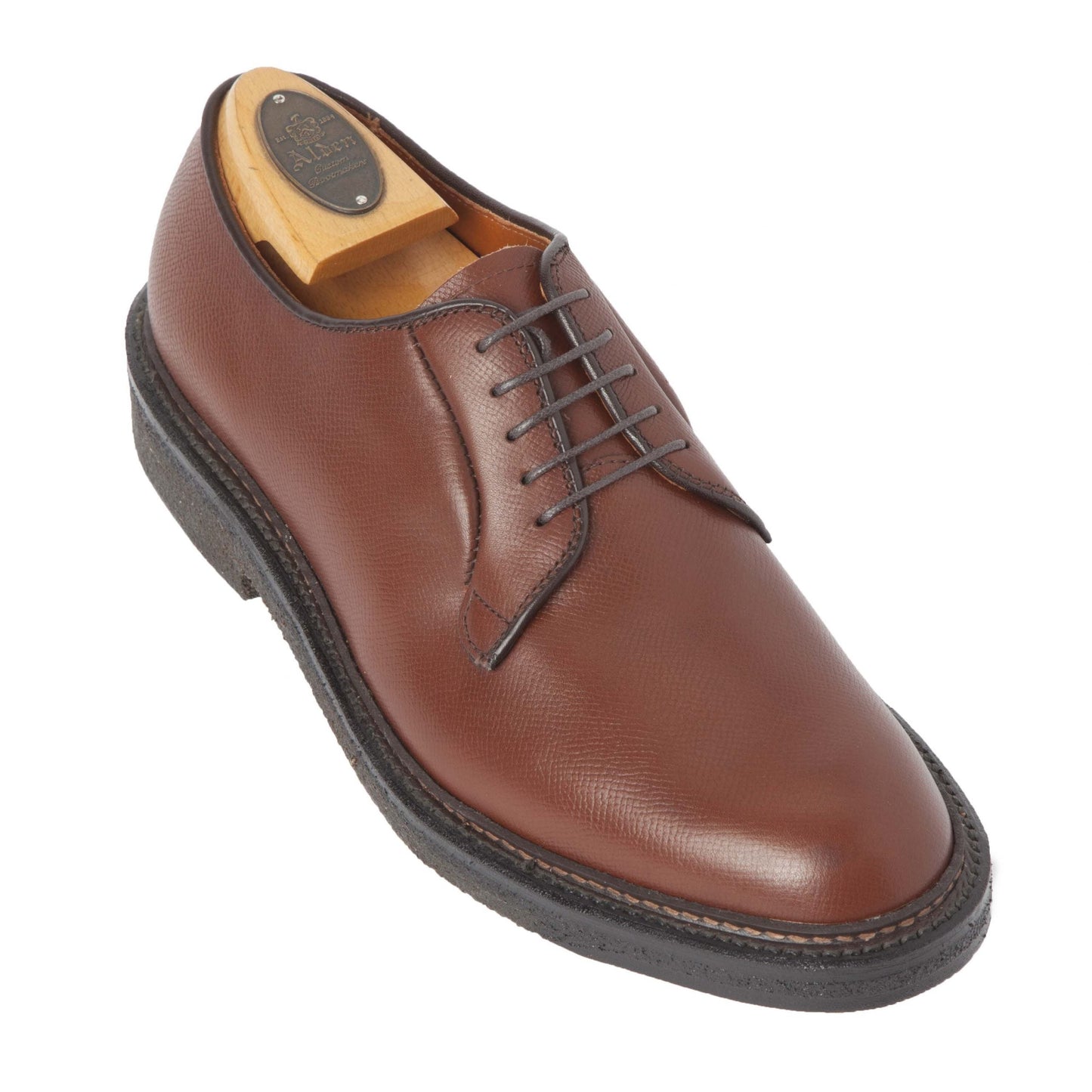 The Alden Madison 947 All Weather Walker is a brown alpine grain calfskin shoe with detailed stitching, black laces, and a textured surface. It includes a wooden shoe tree, has a dark rubber sole, and is crafted on the classic Barrie Last.