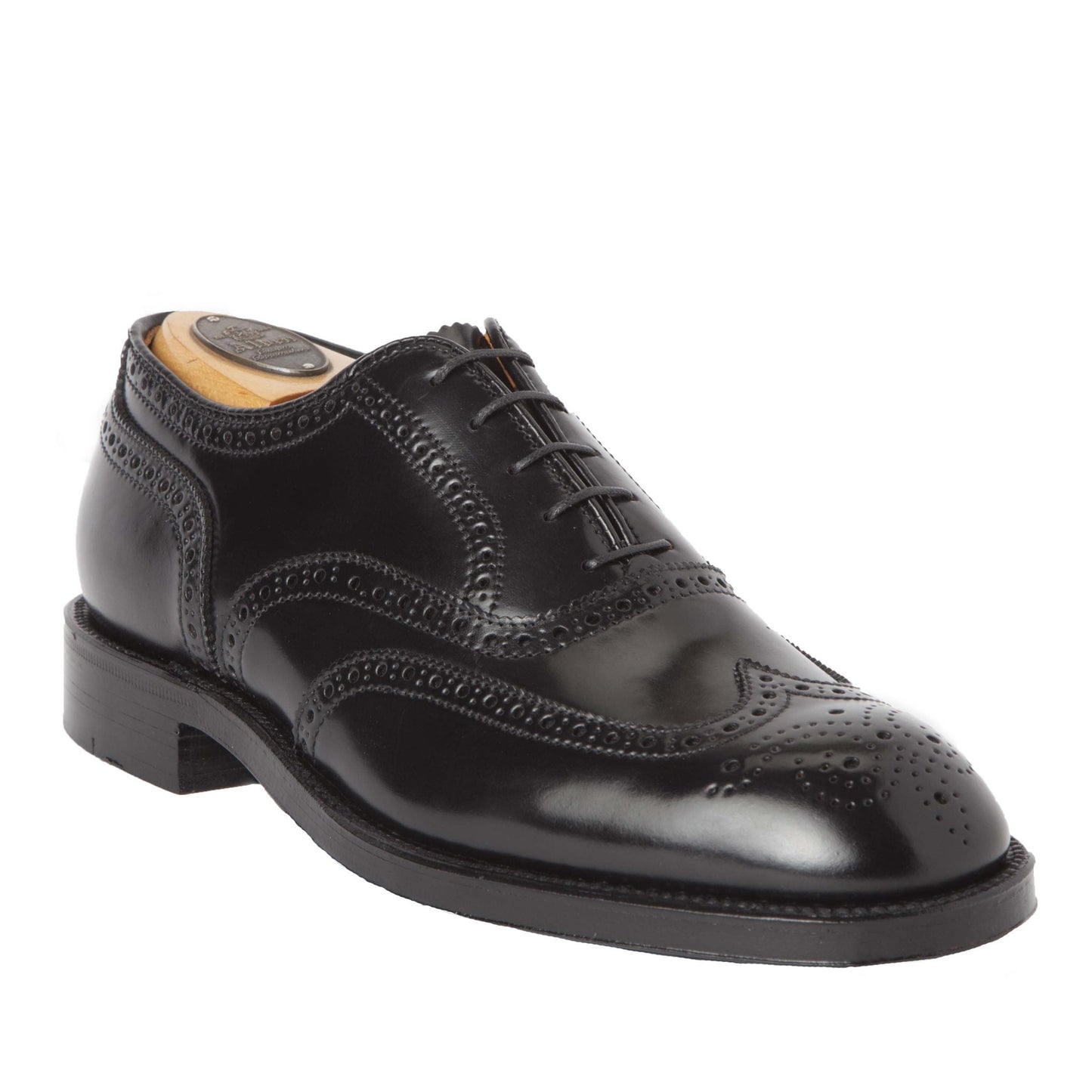 The Alden Madison 9741 - Wing Tip Bal Black Shell Cordovan is a black leather brogue shoe with decorative perforations, a sleek finish, classic lace-up design, wingtip details, a Double Oak Leather Sole, and contains a wooden shoe tree. It rests on a plain white background.