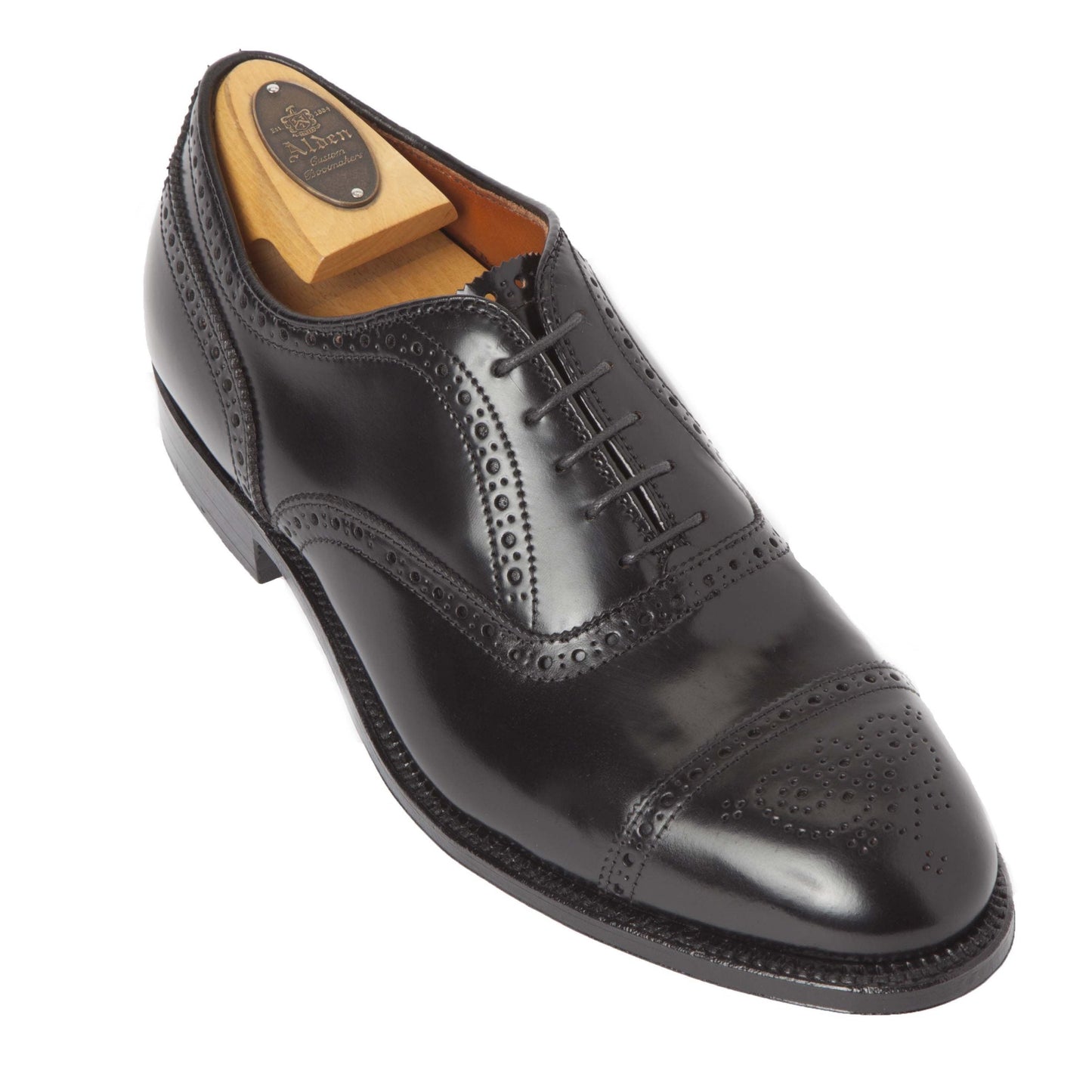 The Alden Madison 9841, a Medallion Cap Toe Bal crafted from Black Shell Cordovan, features intricate brogue detailing on the toe cap and seams. Designed on the Hampton Last with black laces, its showcased with a wooden shoe tree inserted.