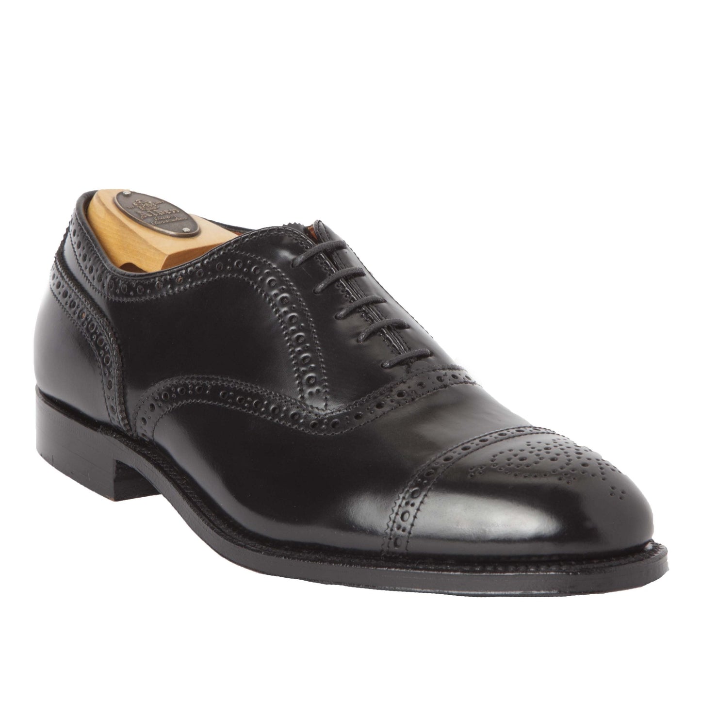 The 9841 Medallion Cap Toe Bal by Alden Madison is a black shell cordovan Oxford shoe with detailed brogue work and a polished finish, crafted on the Hampton Last. It features laces, a low heel, and a Single Oak Leather Sole, showcased on a white background.
