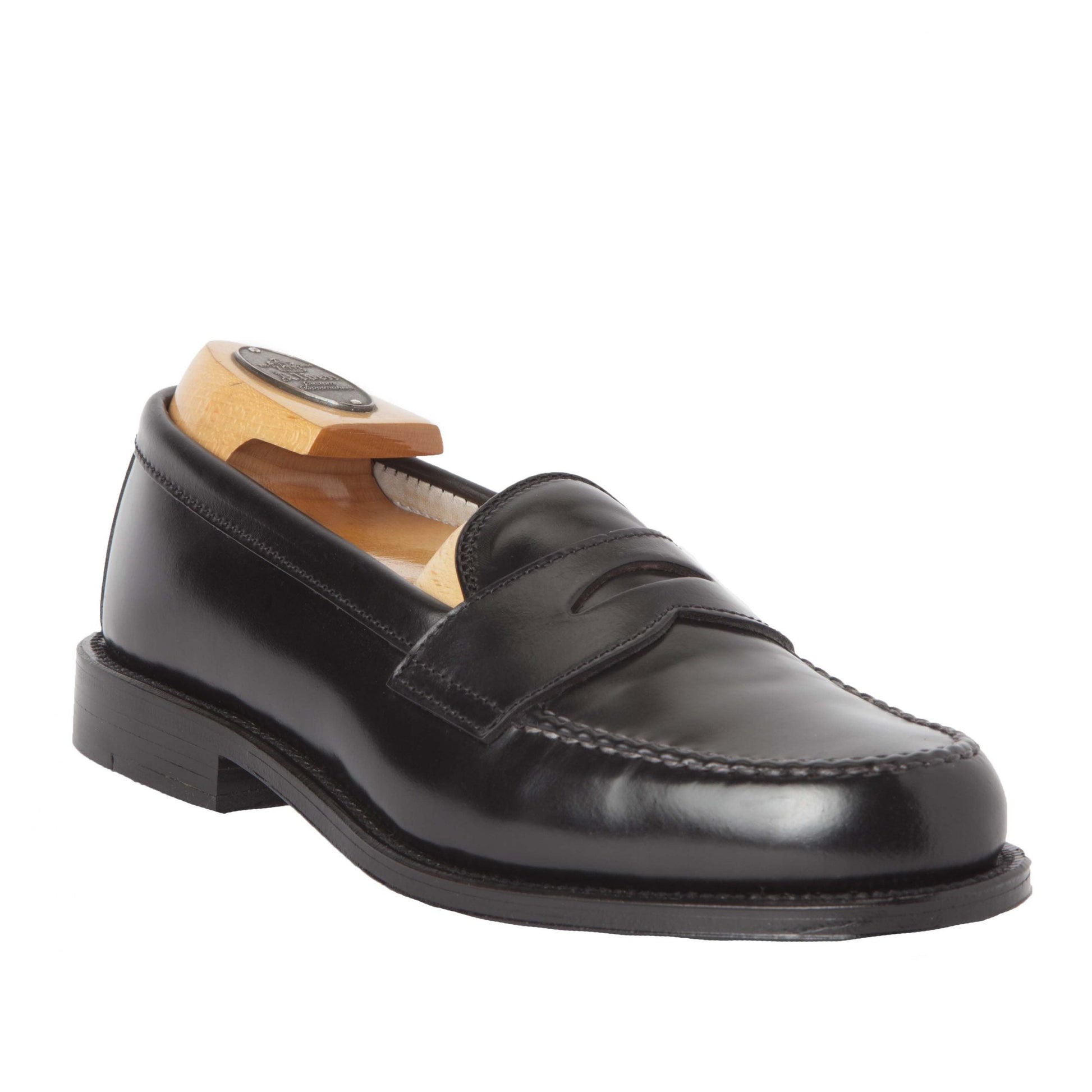 The Alden Madison 987 - Leisure Hand Sewn Black Shell Cordovan loafer, with visible stitching and a wooden shoe tree, is displayed facing slightly right. Its sleek design with a low heel and leather outsole reflects light beautifully, highlighting its elegant craftsmanship.