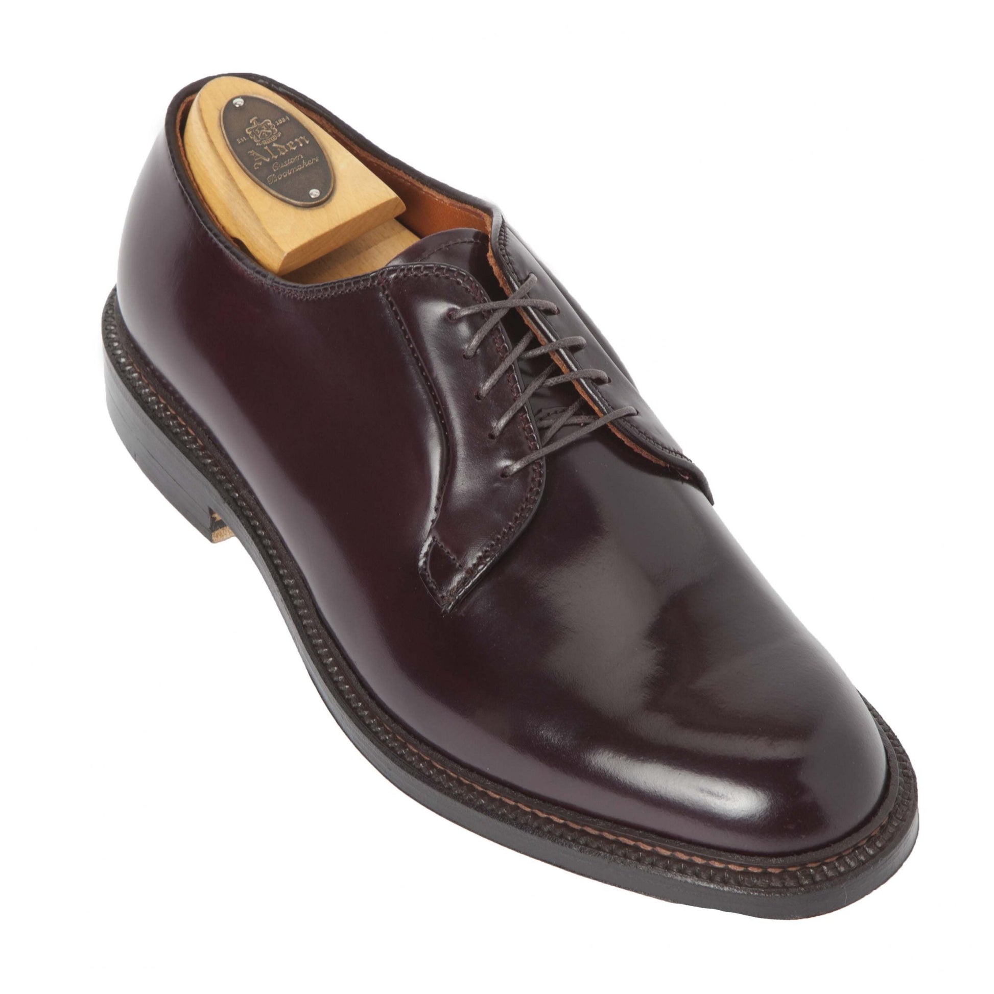 The Alden Madison 990 - Plain Toe Blucher in Color 8 Shell Cordovan exudes timeless sophistication, featuring a polished dark burgundy leather crafted from Shell Cordovan. It rests elegantly on a shoe tree insert with a Barrie Last and complemented by a Double Oak Leather Sole.
