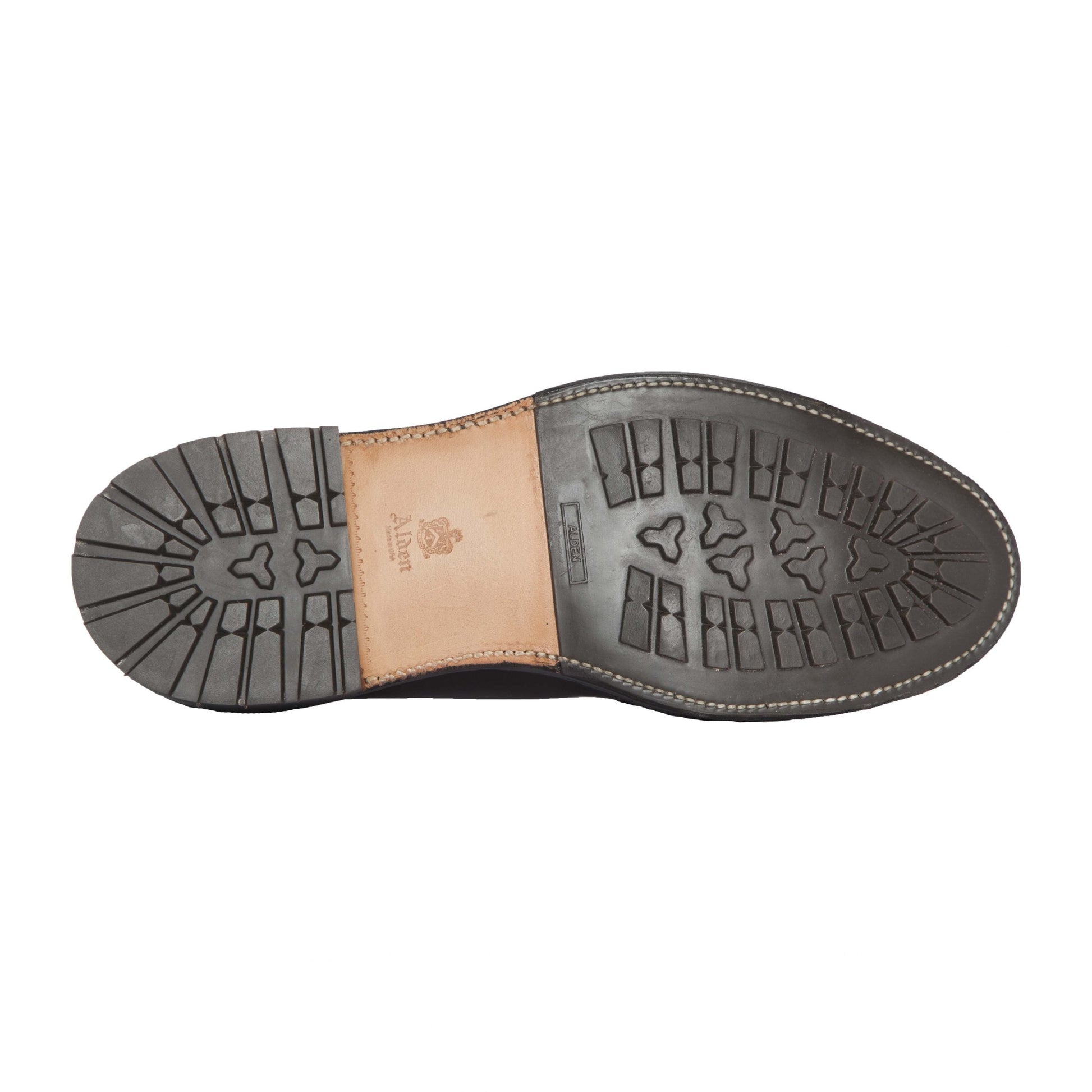 The image shows the sole of the Alden Madison 405C - Original 405 Indy Boot, featuring a rugged Commando Sole for traction. Its predominantly black with a light brown Alden logo in Indy Brown. The edge stitching showcases craftsmanship, ideal for leather enthusiasts favoring durability.