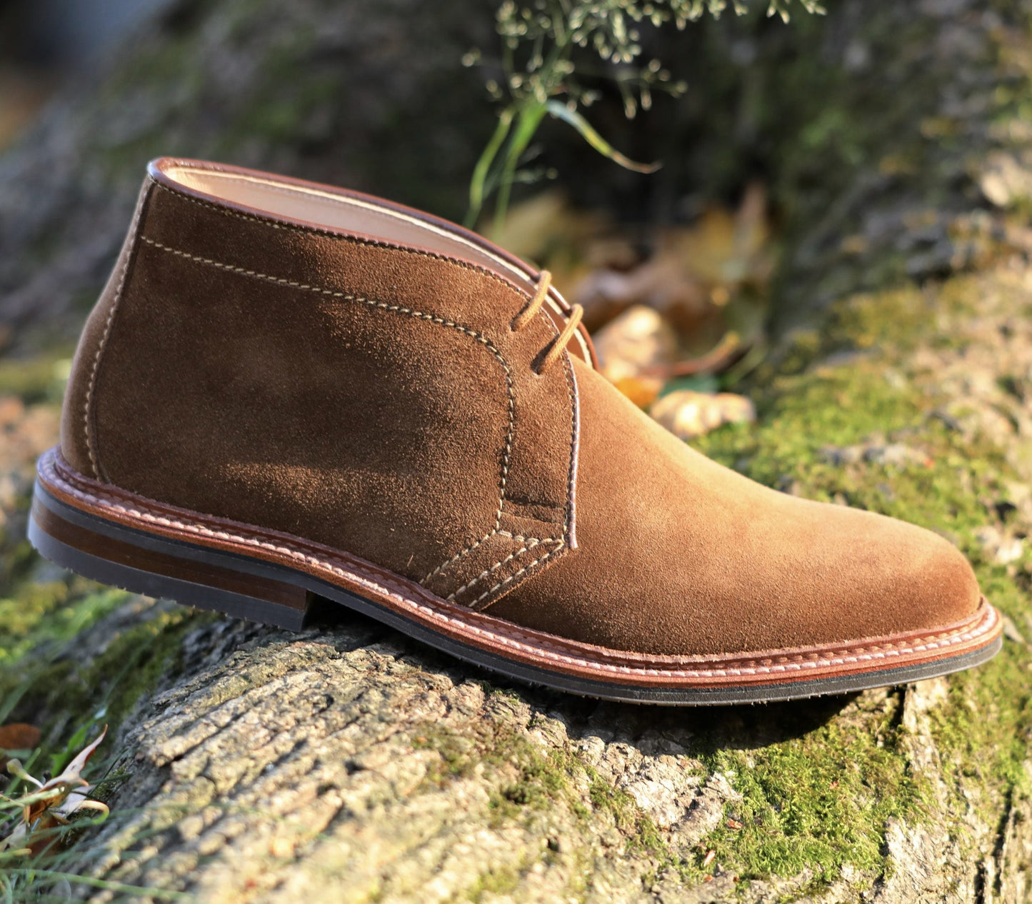 A brown Alden Madison 1593L chukka boot in snuff suede, crafted on the Barrie Last with an L3 sole, sits gracefully on a mossy tree trunk. Its visible stitching and layered sole blend rugged charm with elegance.