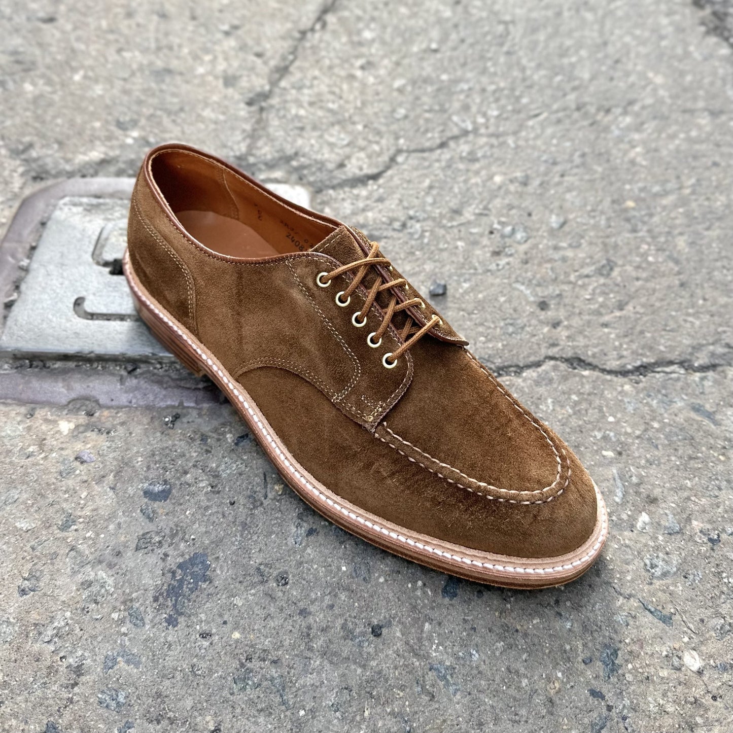 The Quickley in Snuff Suede by Alden Madison, featuring detailed stitching, brown suede with matching laces, and a light-colored sole on the Barrie Last, is showcased on a textured concrete surface.