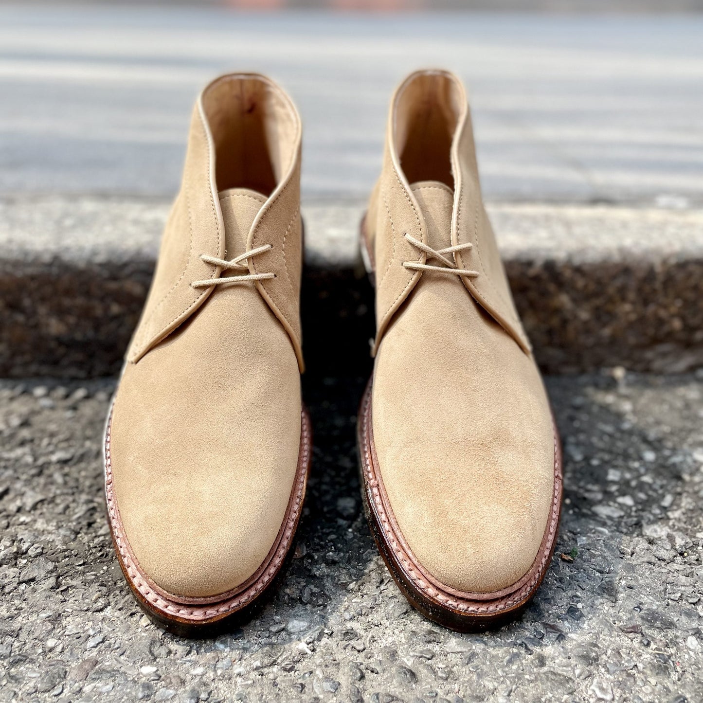 The Alden Madison 14580 - Desert Chukka Boot in Tan Suede rests on a textured surface, showcasing its classic design with laces and a crepe sole that highlights its sleek and polished appearance.