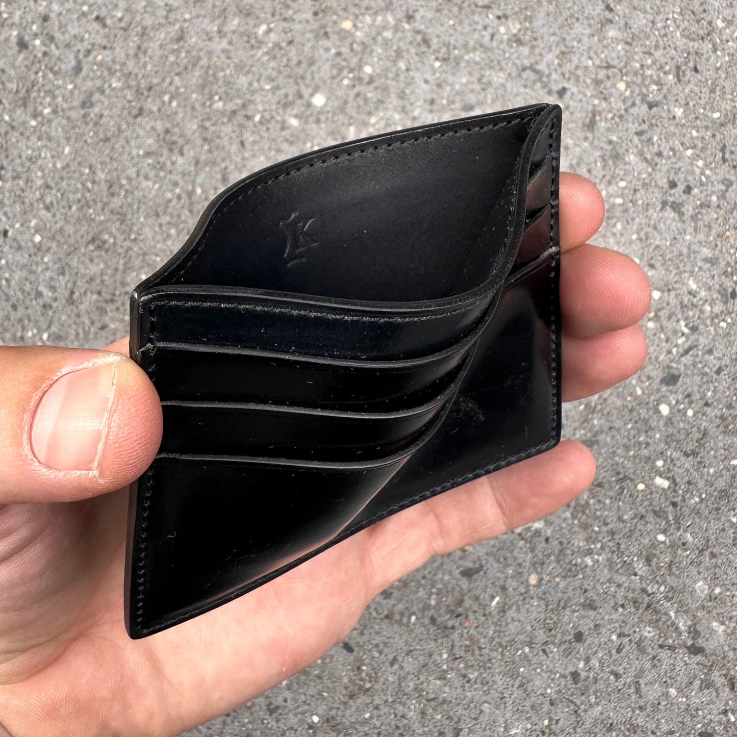 A person holds an Alden Madison LG 6009 - Alden Black Shell Credit Card Holder with visible card slots, highlighting its 6 pockets. The textured gray background mirrors the timeless elegance of Shell Cordovan leather reminiscent of an Alden Shoe.
