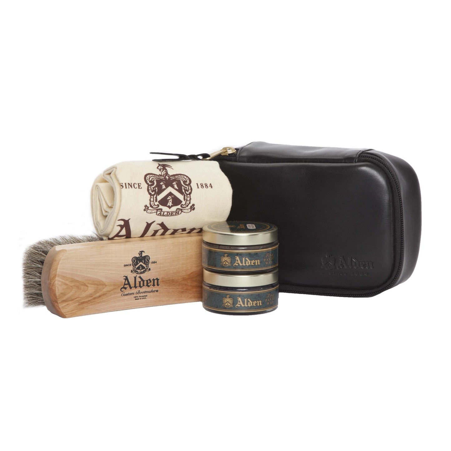 The Alden Madison Polish Kit is a sleek leather care set with a calfskin carry case, including a polishing cloth, wooden horse hair brush, and two tins of Alden paste wax. All items are elegantly branded Alden and arranged neatly in front of the pouch.