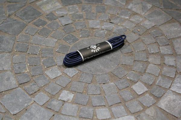 A black Alden Madison Shoe Lace Guarded Goods, 27 inches long with a paper label, rests on a stone tile floor set in a circular mosaic design.